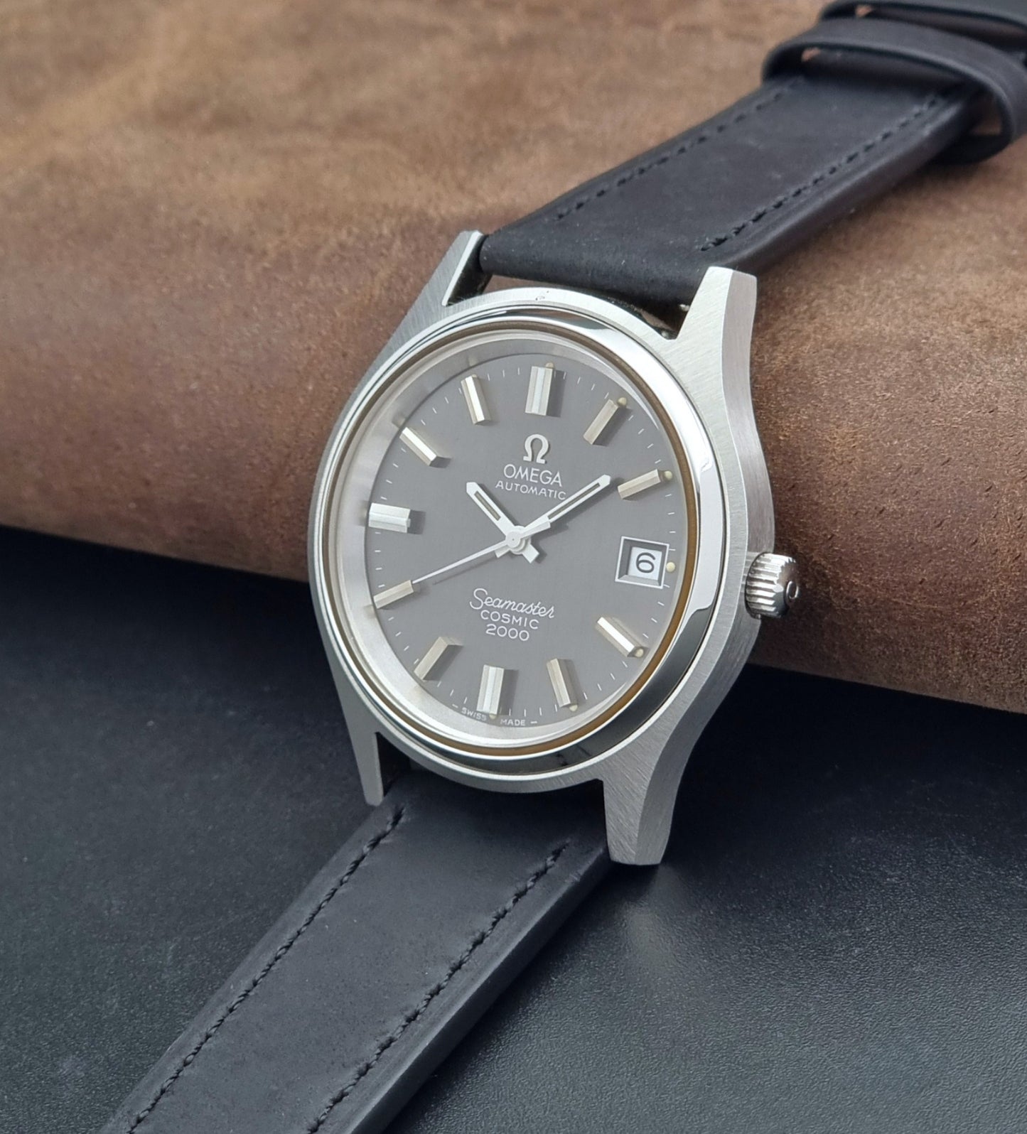 Vintage Omega Wristwatch Seamaster Cosmic 2000 Jumbo 166.128 grey dial with black leather strap on a dark gray background crown view