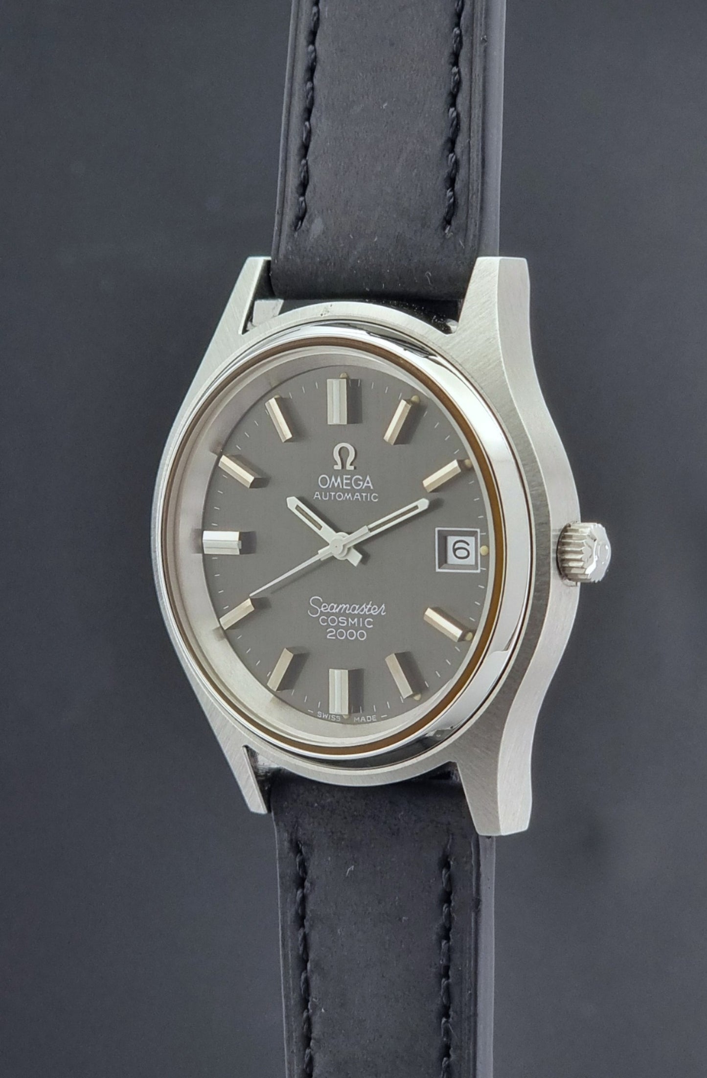 Vintage Omega Wristwatch Seamaster Cosmic 2000 Jumbo 166.128 grey dial with black leather strap on a dark gray background crown profile view