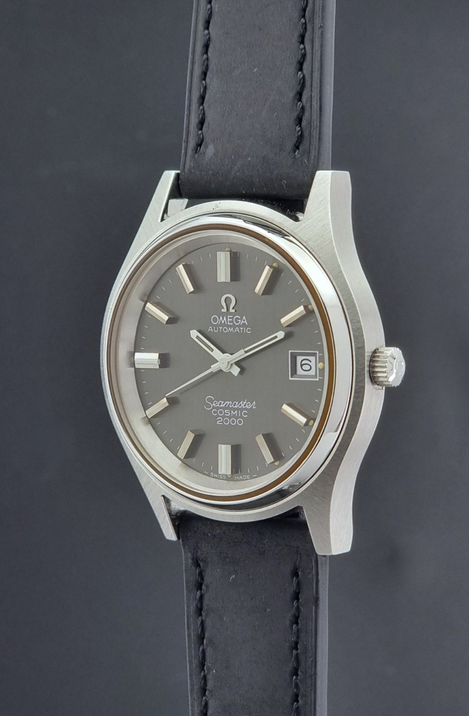 Vintage Omega Wristwatch Seamaster Cosmic 2000 Jumbo 166.128 grey dial with black leather strap on a dark gray background crown profile view