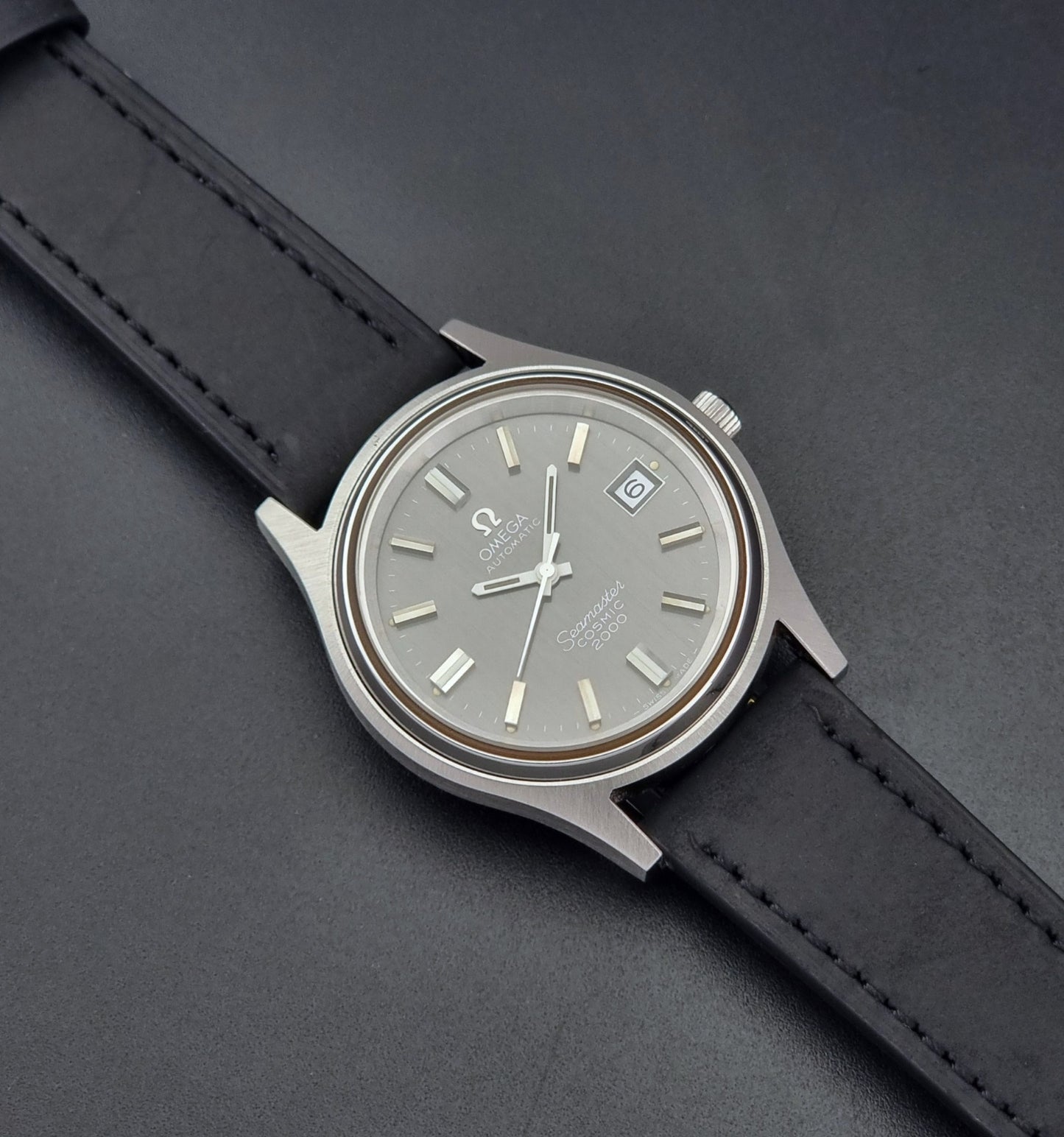 Vintage Omega Wristwatch Seamaster Cosmic 2000 Jumbo 166.128 grey dial with black leather strap on a dark gray background dial