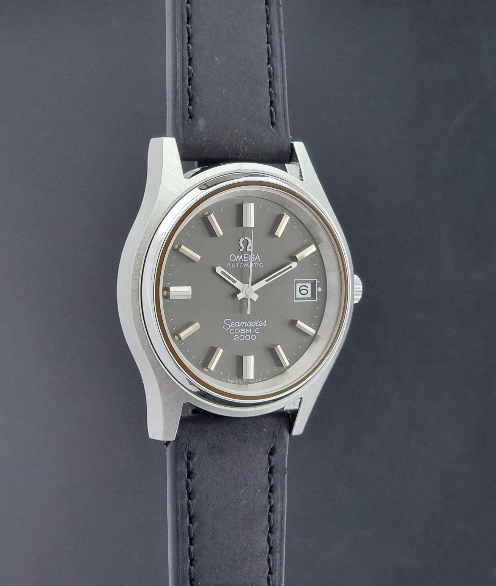 Vintage Omega Wristwatch Seamaster Cosmic 2000 Jumbo 166.128 grey dial with black leather strap on a dark gray background side profile view