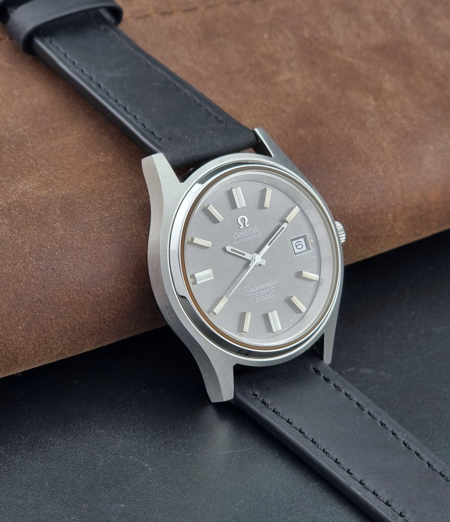 Vintage Omega Wristwatch Seamaster Cosmic 2000 Jumbo 166.128 grey dial with black leather strap on a dark gray background side view