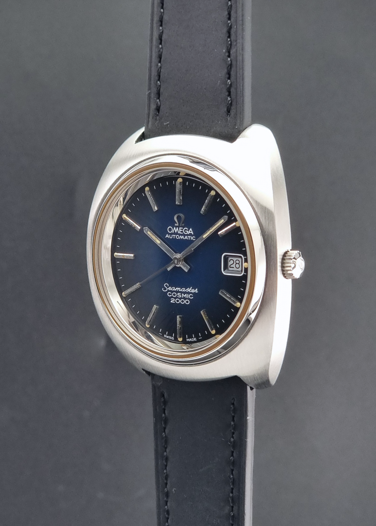 Vintage Omega Wristwatch 166.132 Seamaster Cosmic 2000 with a polished silver-tone oval case, dark blue dial, and black leather strap, shown against a dark gray background.
