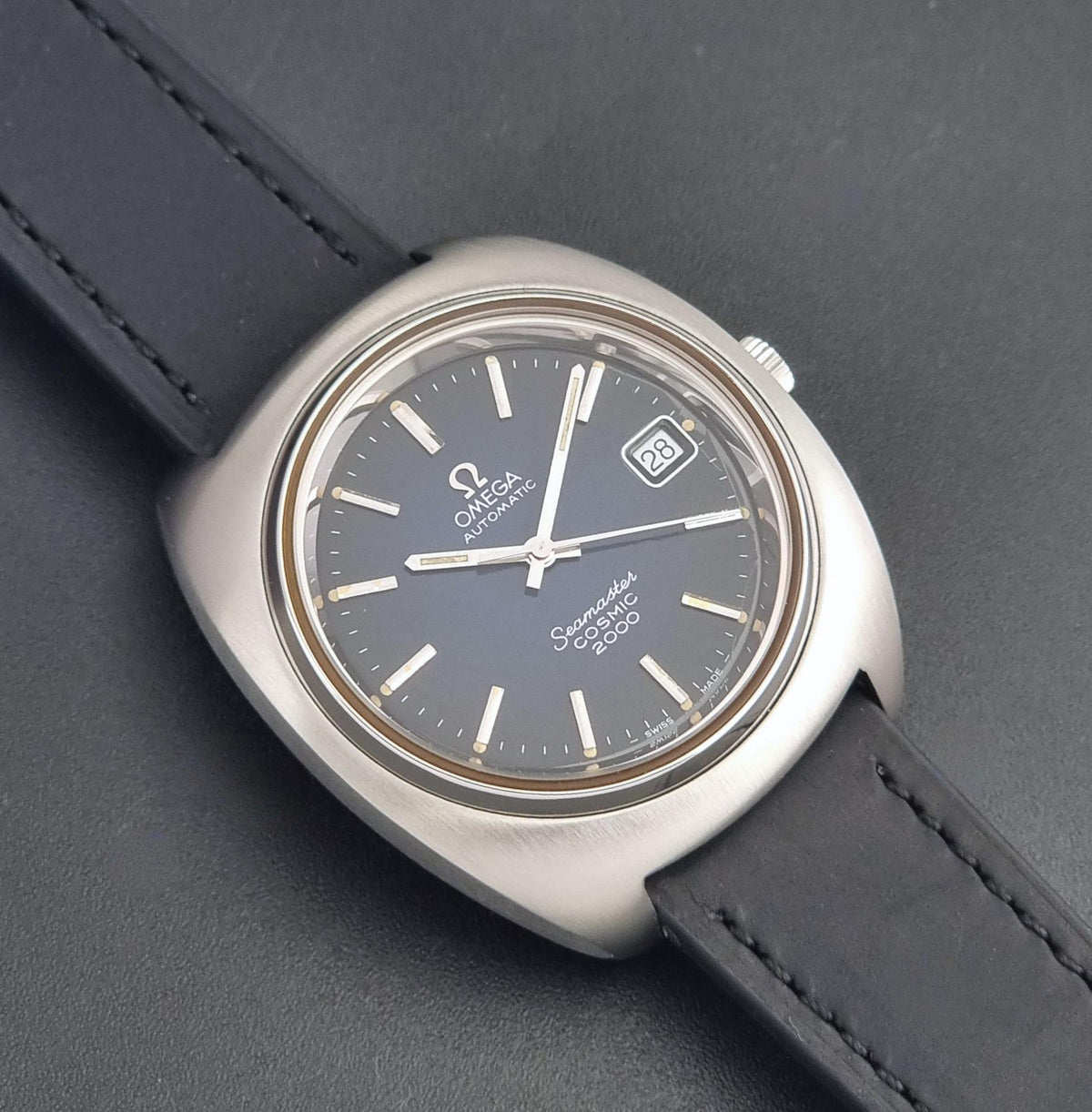 Vintage Omega Wristwatch 166.132 Seamaster Cosmic 2000 with a dark gray dial, brushed stainless steel case, and black leather strap, shown on a dark gray textured background.