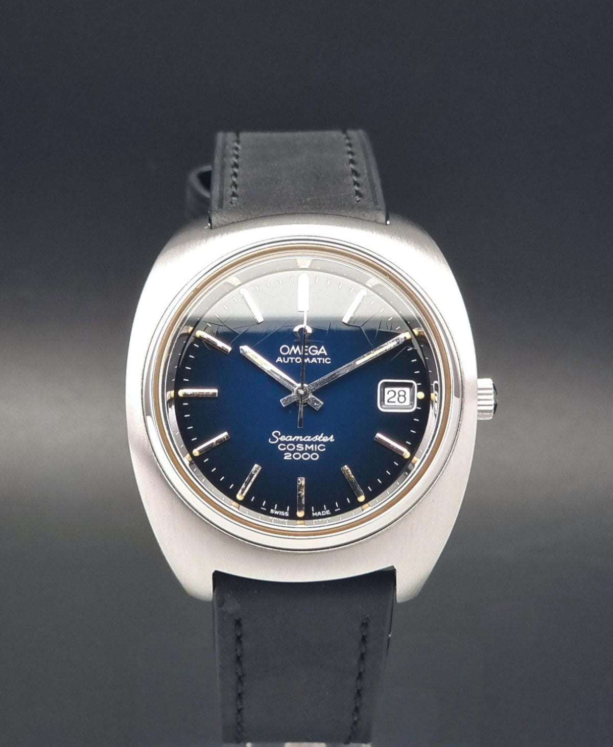 Vintage Omega Wristwatch 166.132 Seamaster Cosmic 2000 with a silver-tone stainless steel case, a deep blue dial, and a black leather strap, shown against a dark gray background.