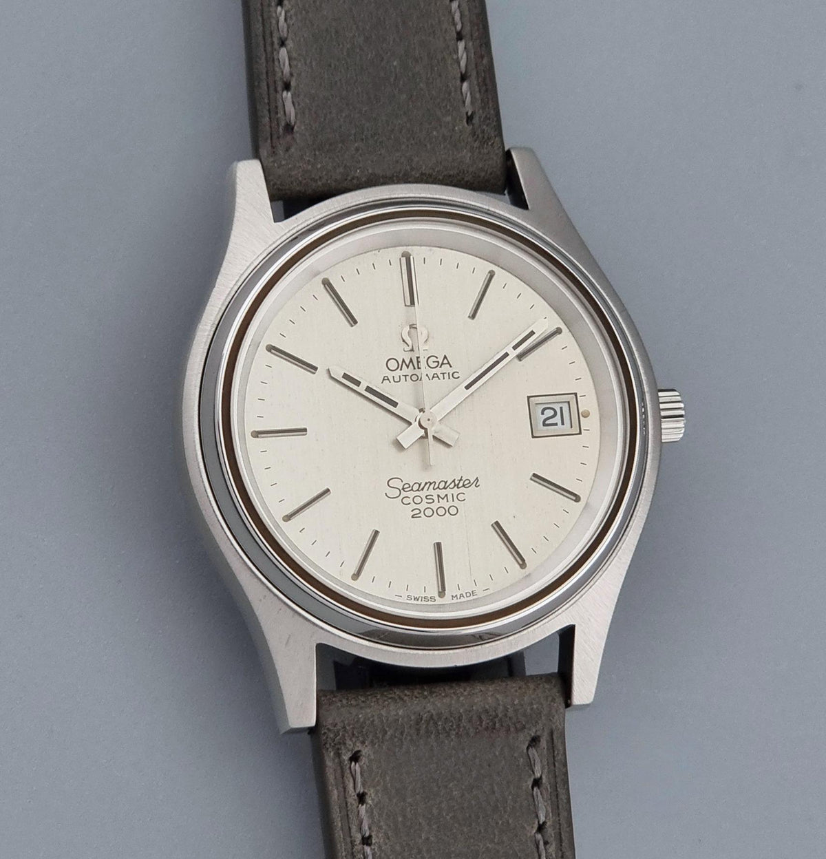 Vintage Omega Wristwatch 166.128 Seamaster Cosmic 2000 with a silver stainless steel case, white dial, and a dark gray leather strap, shown on a neutral gray background.