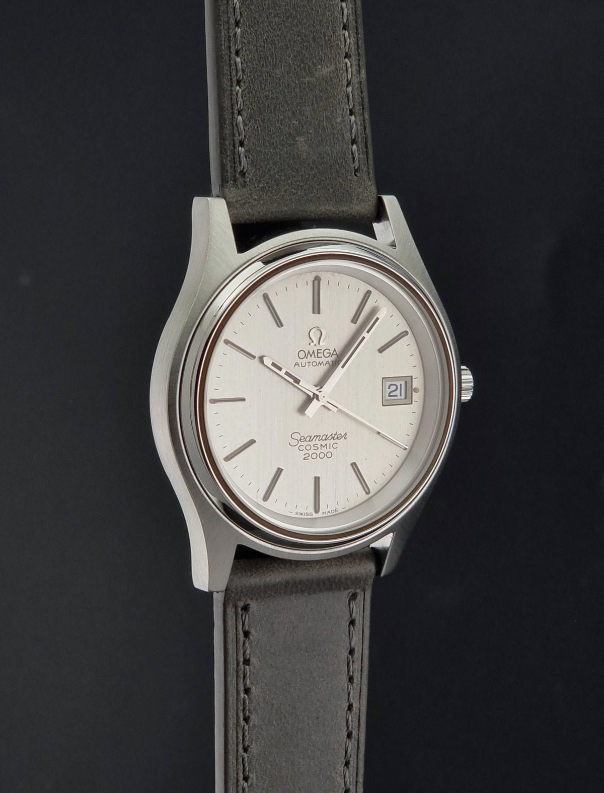Vintage Omega Wristwatch 166.128 Seamaster Cosmic 2000 with a silver-toned oval case, white dial, and dark gray leather strap, shown against a dark background.