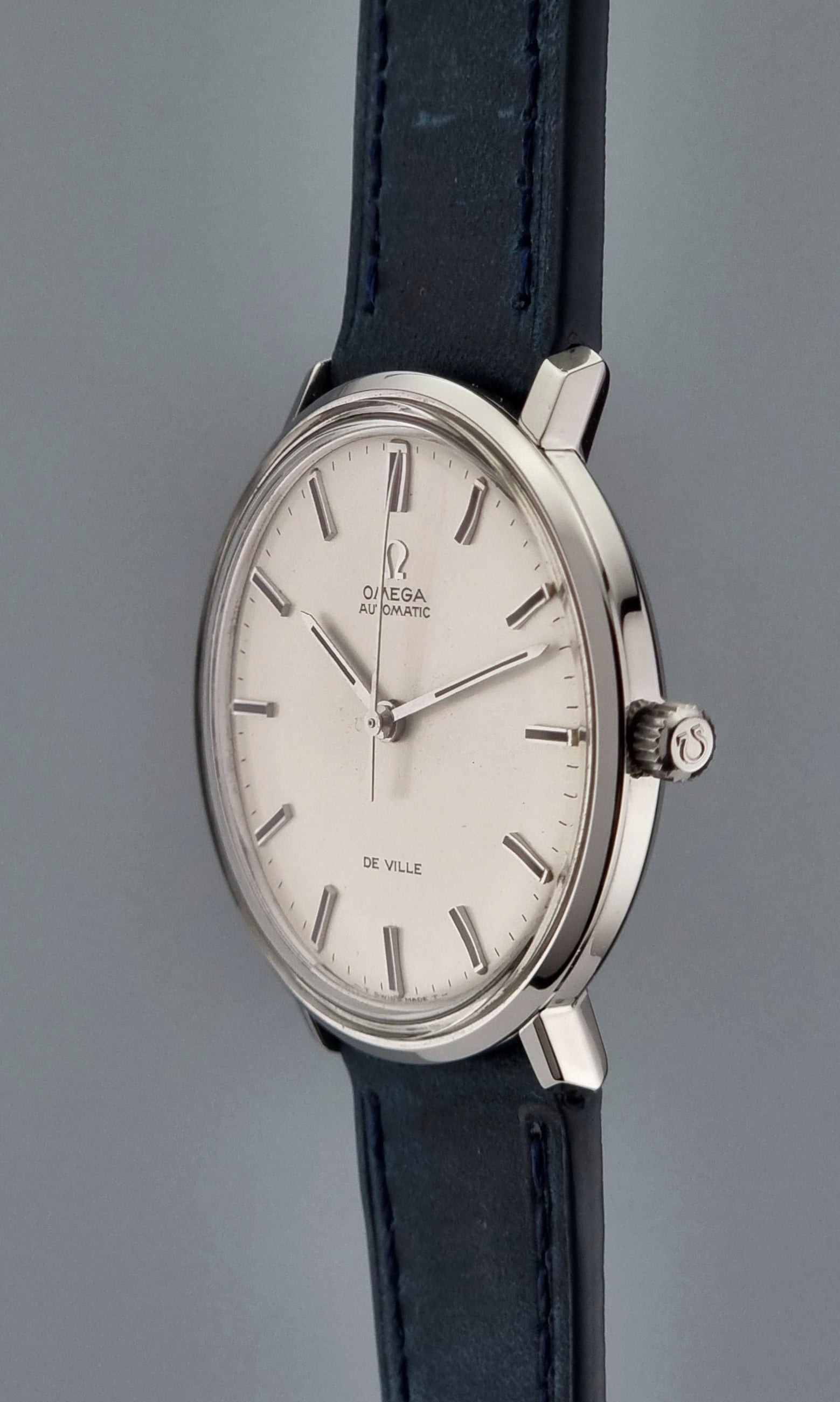 Vintage Omega De-Ville watch with a silver case and black leather strap on a gray background