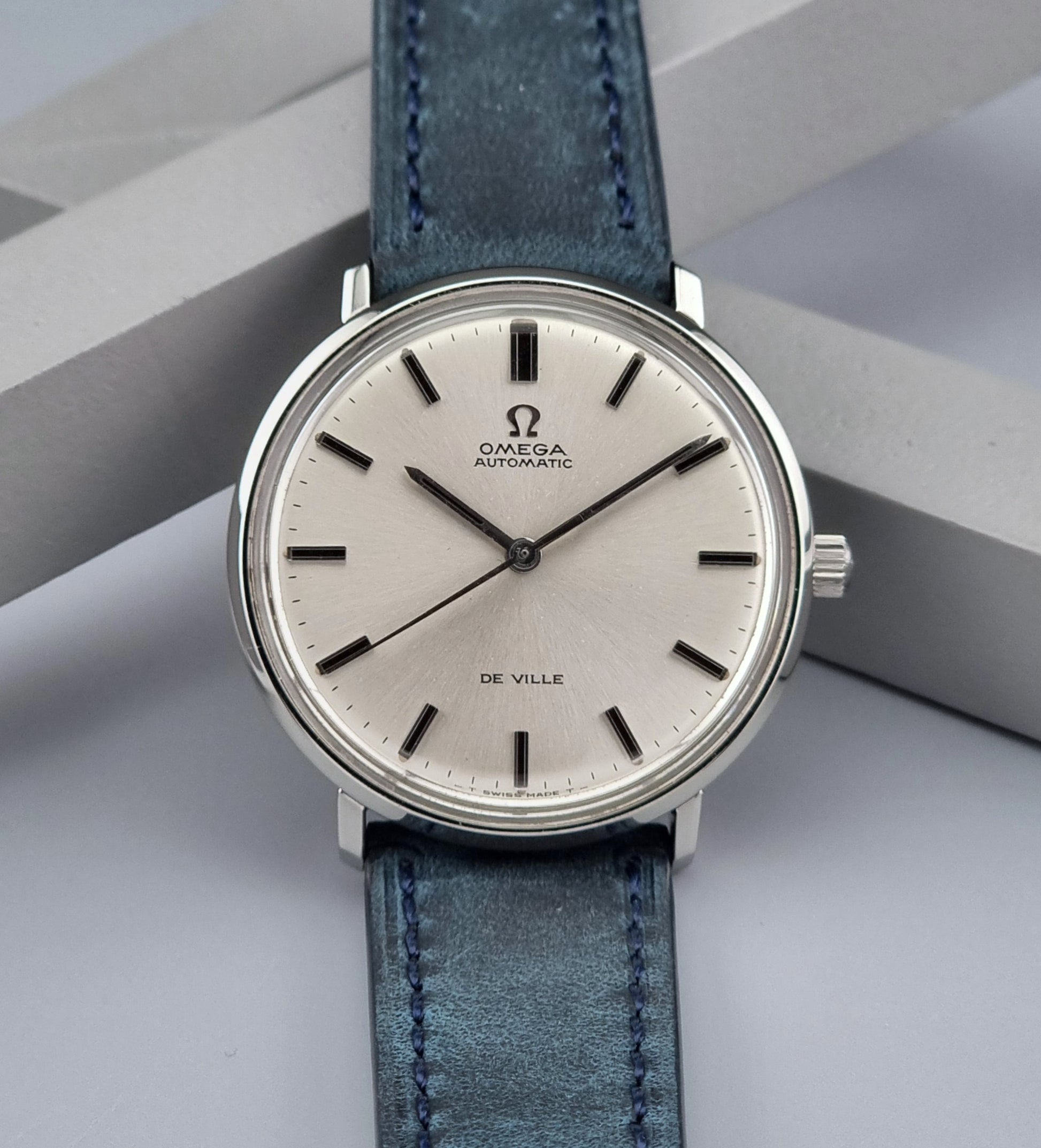 Vintage Omega De-Ville watch with blue leather strap on a gray background