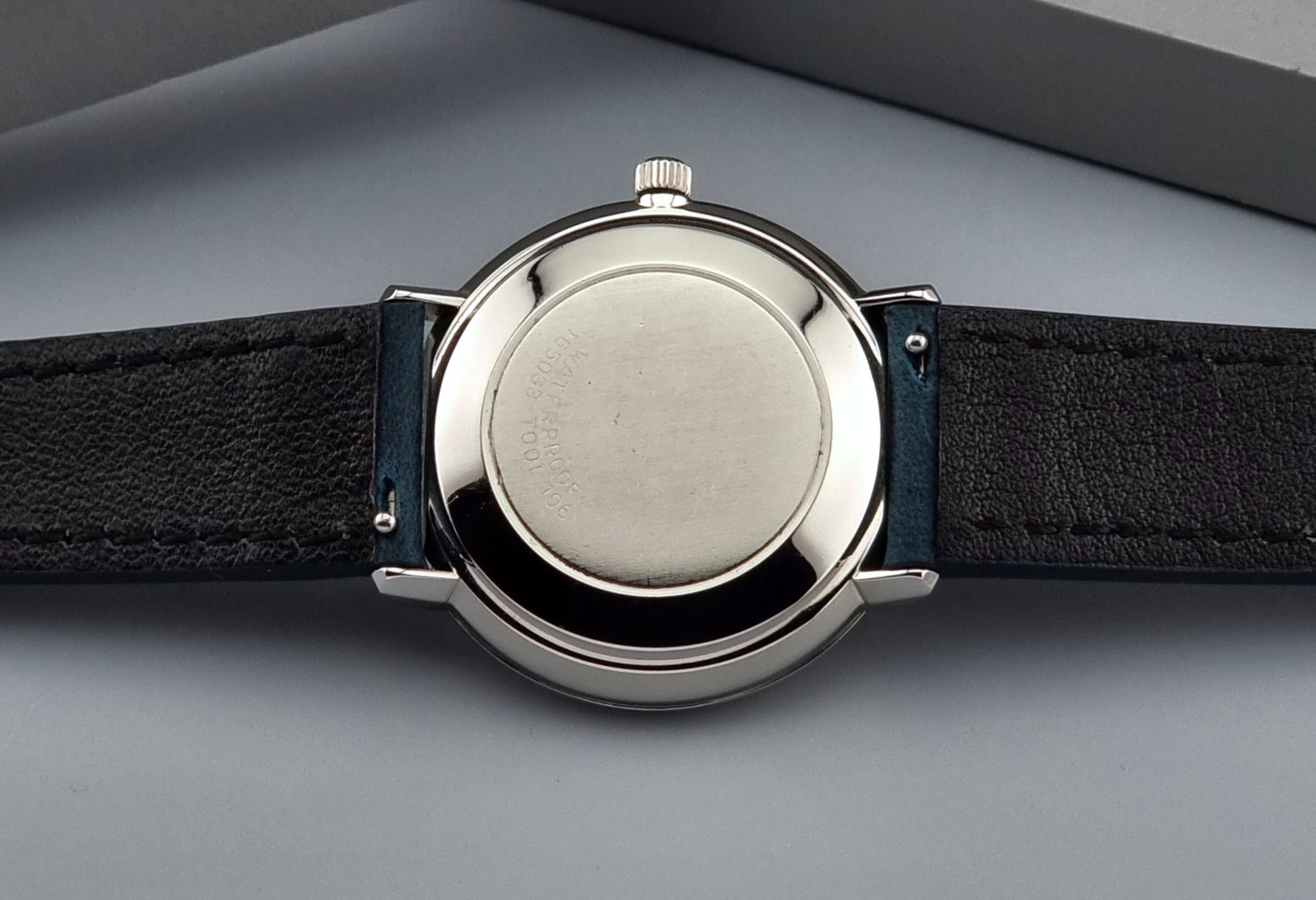 Close-up of a Vintage Omega De-Ville case back with a black leather strap on a gray background