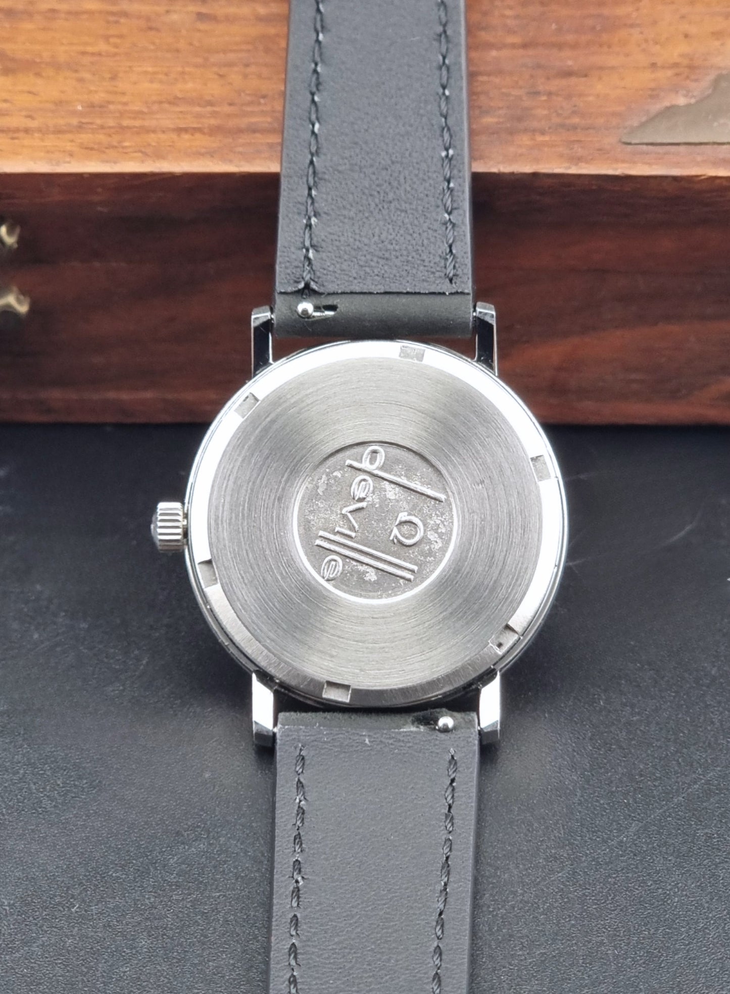 Vintage Omega  De-Ville 166.0086 wristwatch with a silver-toned case, and black leather strap, photographed on a dark background back view