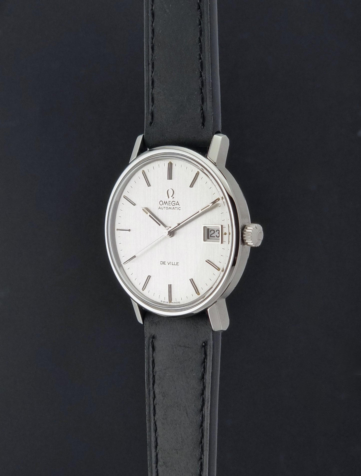 Vintage Omega  De-Ville 166.0086 wristwatch with a silver-toned case, and black leather strap, photographed on a dark background crown profile view