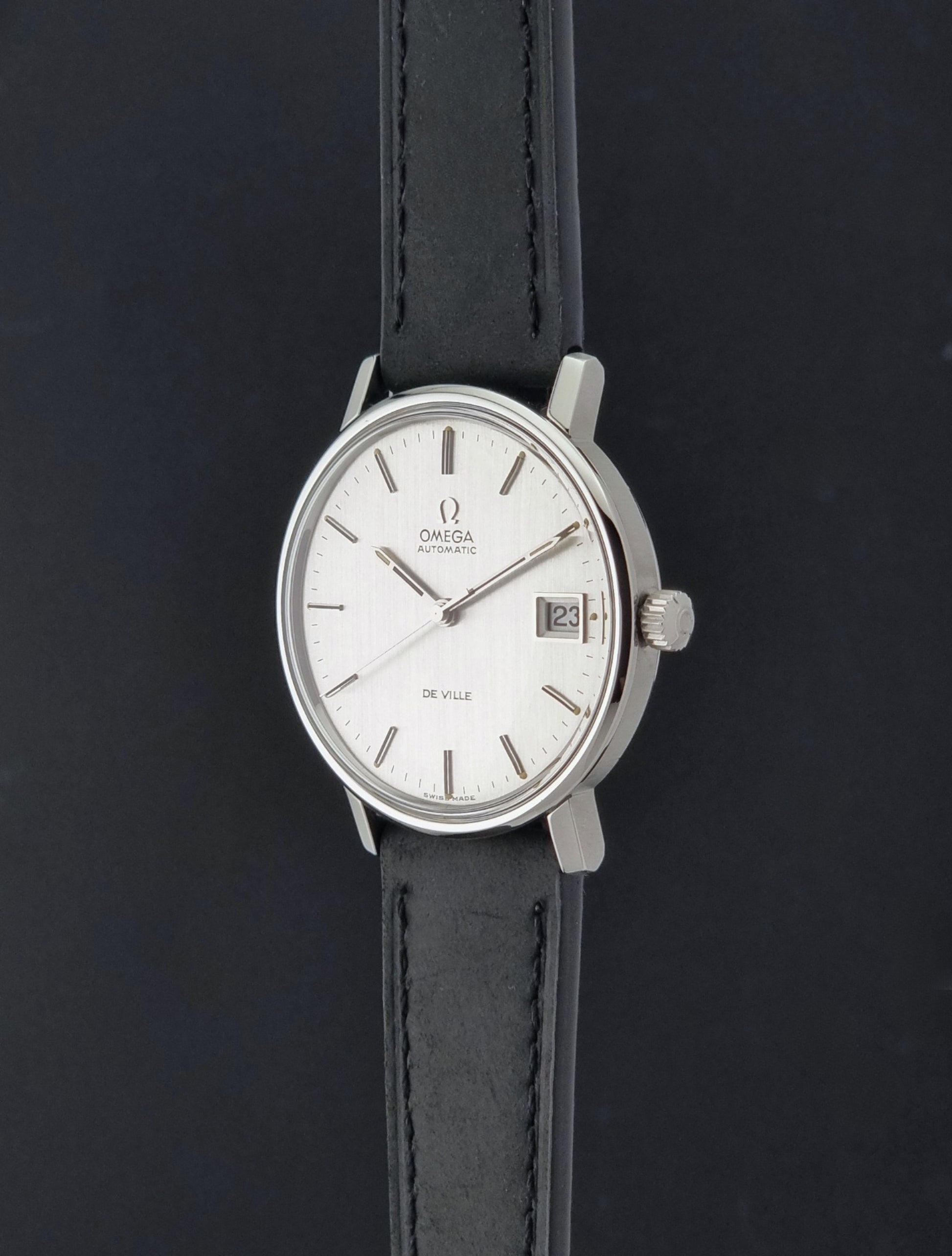 Vintage Omega  De-Ville 166.0086 wristwatch with a silver-toned case, and black leather strap, photographed on a dark background crown profile view