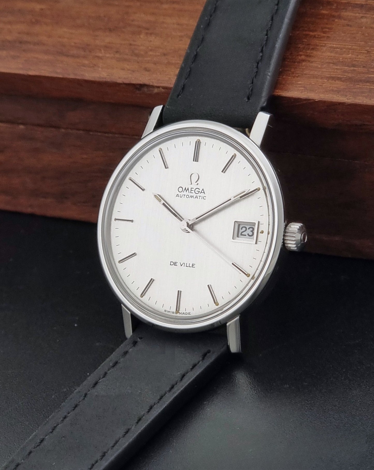 Vintage Omega  De-Ville 166.0086 wristwatch with a silver-toned case, and black leather strap, photographed on a dark background crown view