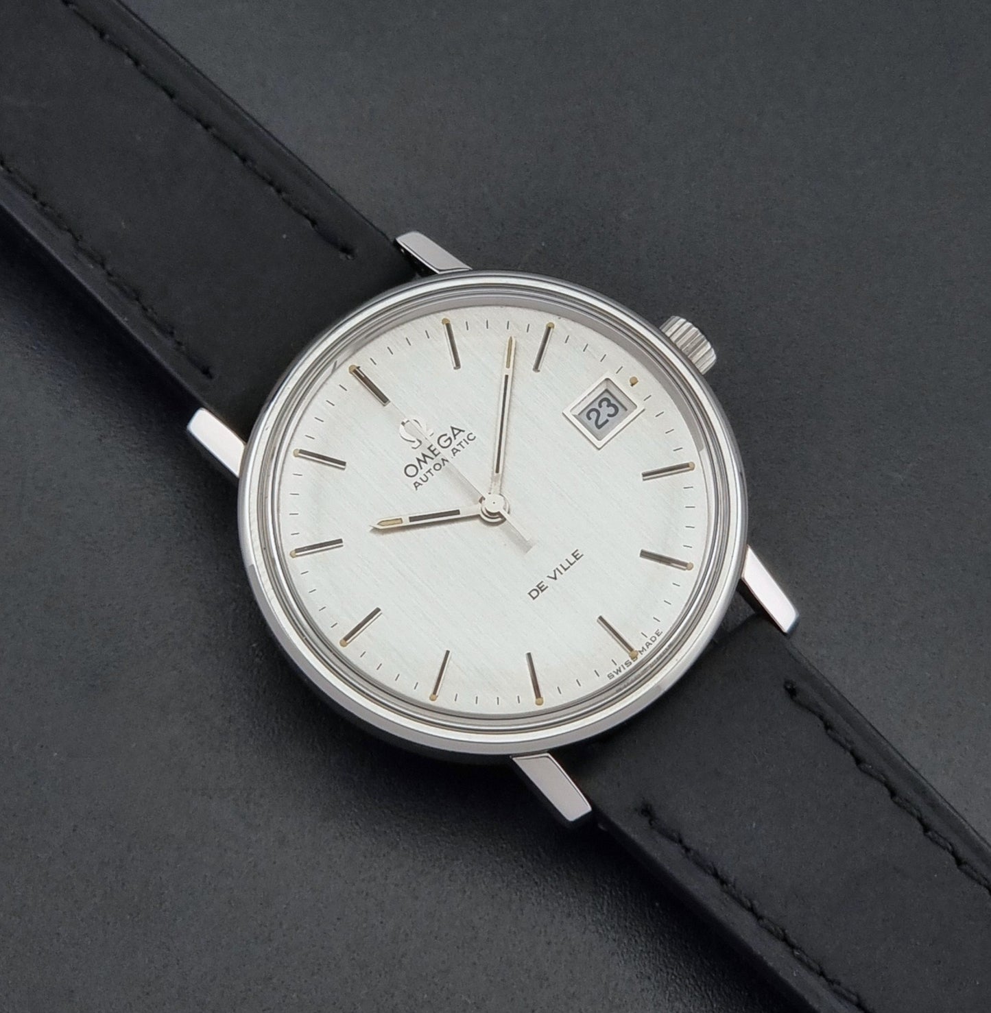 Vintage Omega  De-Ville 166.0086 wristwatch with a silver-toned case, and black leather strap, photographed on a dark background close up dial view