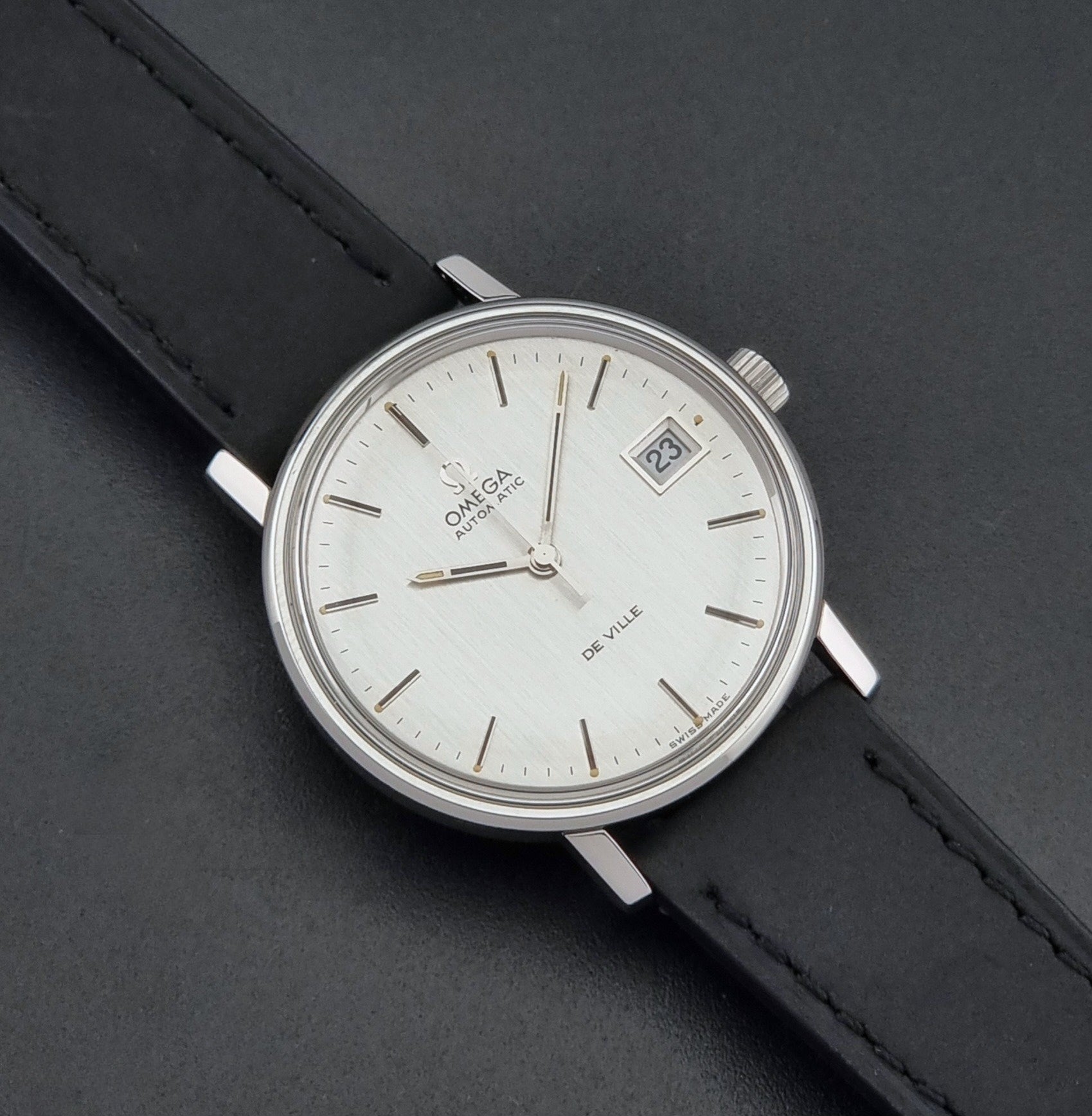 Vintage Omega  De-Ville 166.0086 wristwatch with a silver-toned case, and black leather strap, photographed on a dark background close up dial view