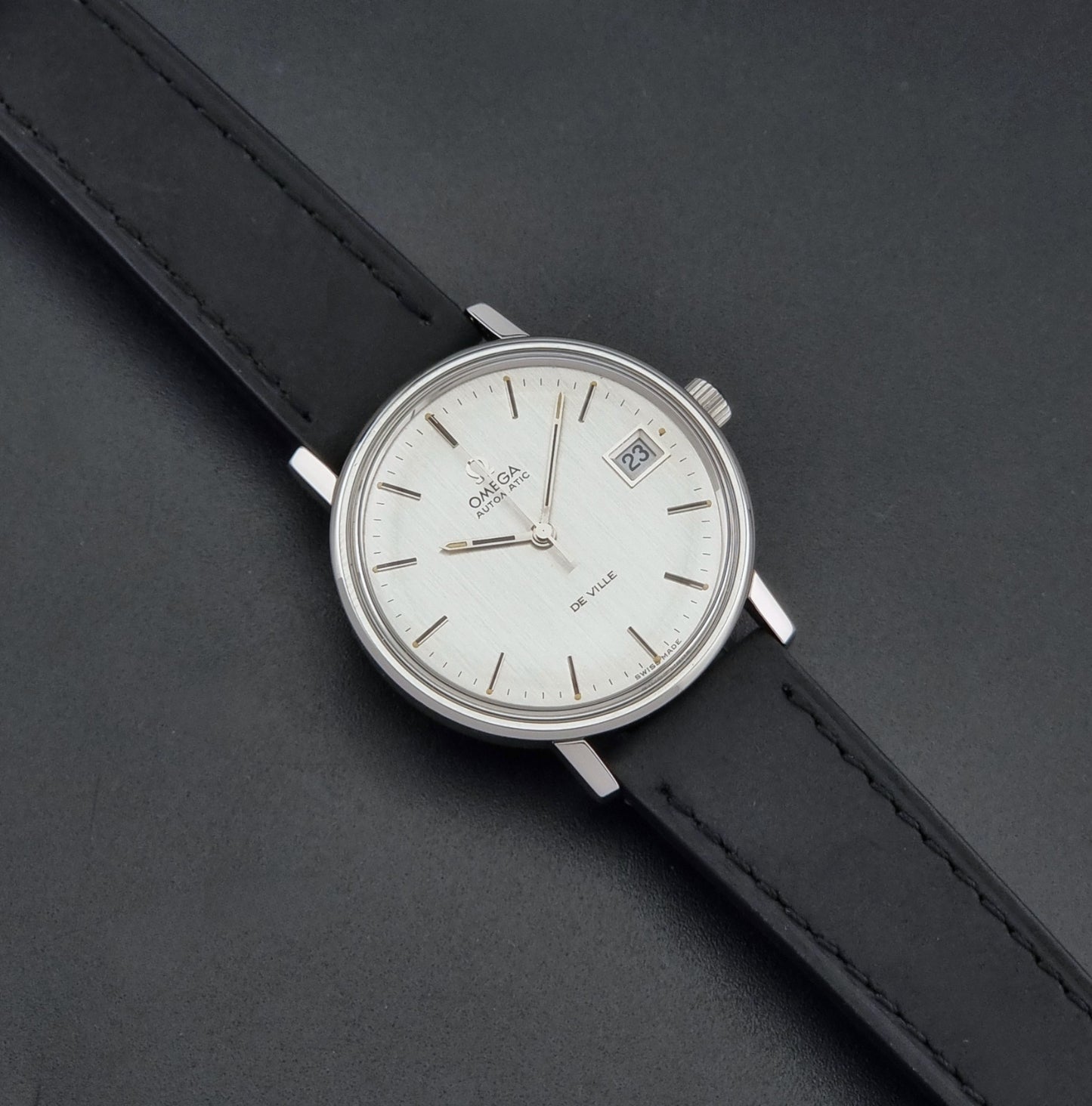 Vintage Omega  De-Ville 166.0086 wristwatch with a silver-toned case, and black leather strap, photographed on a dark background dial