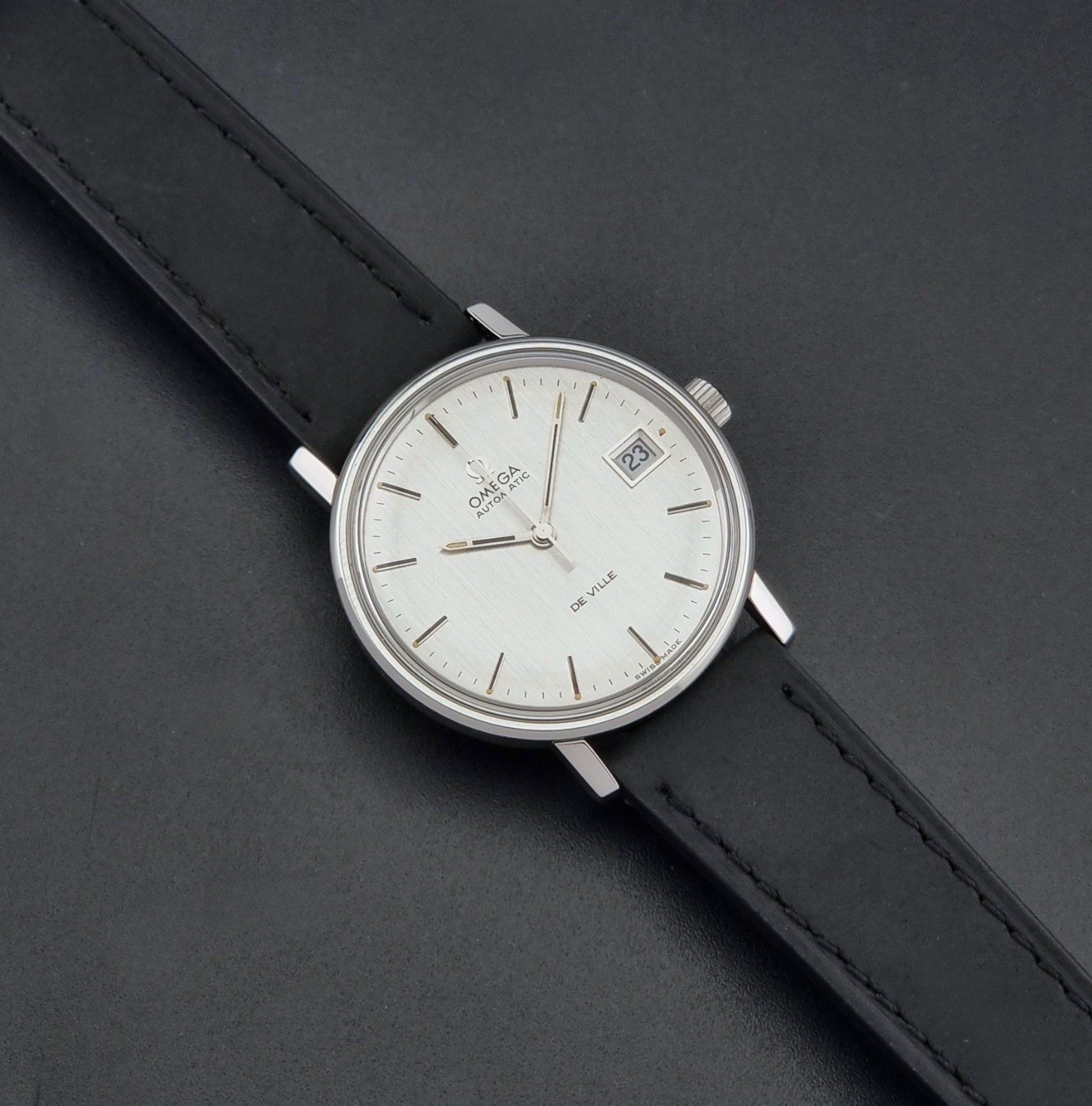 Vintage Omega  De-Ville 166.0086 wristwatch with a silver-toned case, and black leather strap, photographed on a dark background dial