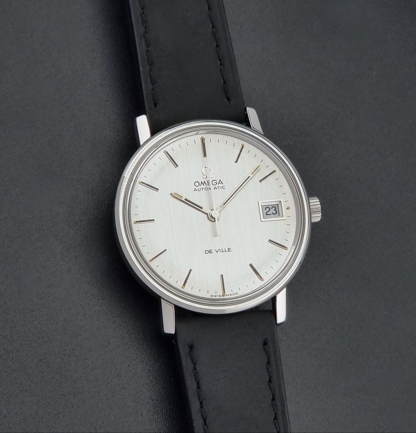 Vintage Omega  De-Ville 166.0086 wristwatch with a silver-toned case, and black leather strap, photographed on a dark background front view