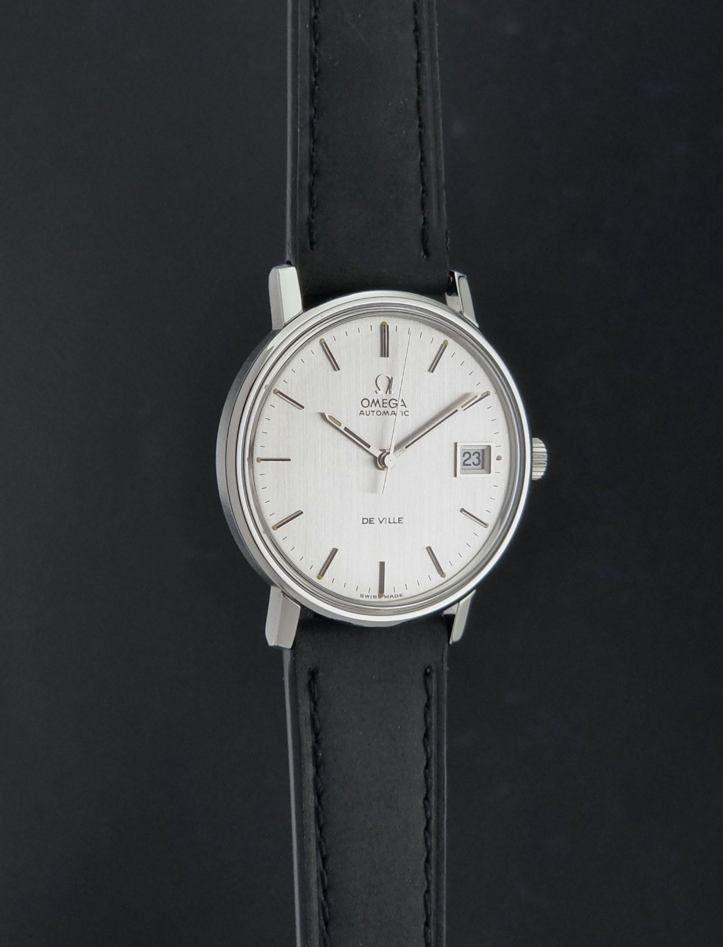 Vintage Omega  De-Ville 166.0086 wristwatch with a silver-toned case, and black leather strap, photographed on a dark background side profile view