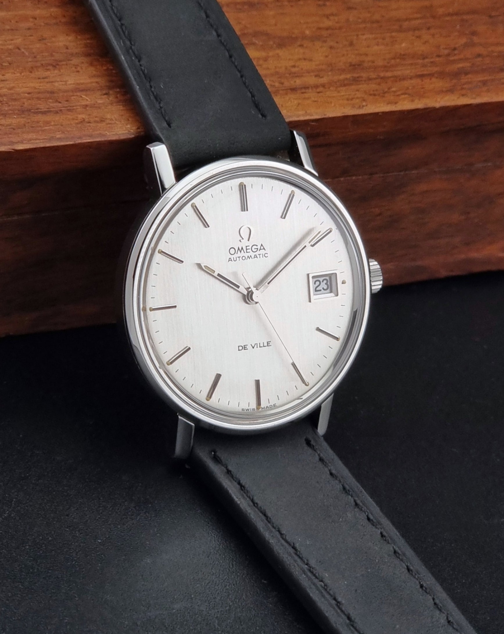 Vintage Omega  De-Ville 166.0086 wristwatch with a silver-toned case, and black leather strap, photographed on a dark background side view