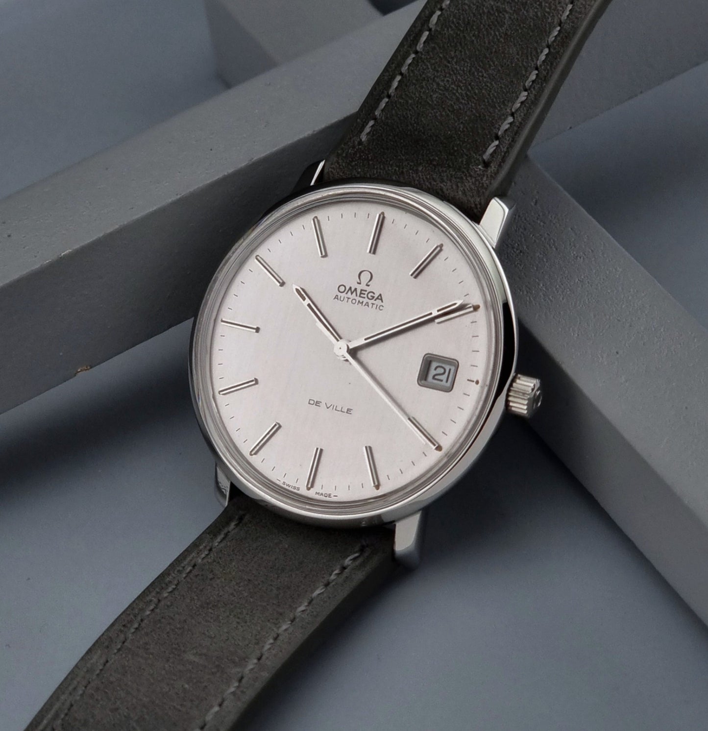 Vintage Omega De-ville 166.0134 wristwatch with a silver dial and dark leather strap on a gray background crown view