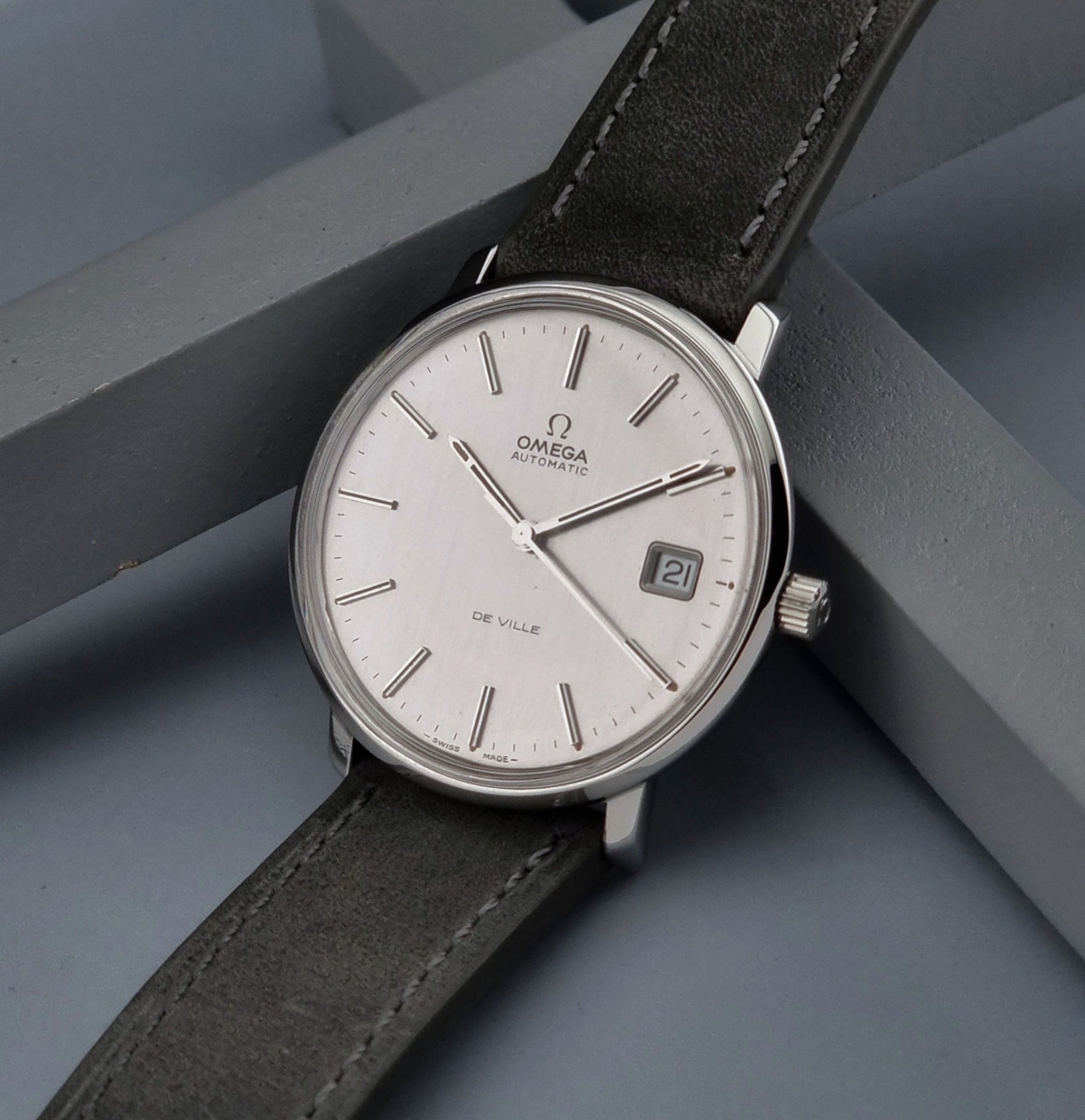 Vintage Omega De-ville 166.0134 wristwatch with a silver dial and dark leather strap on a gray background crown view