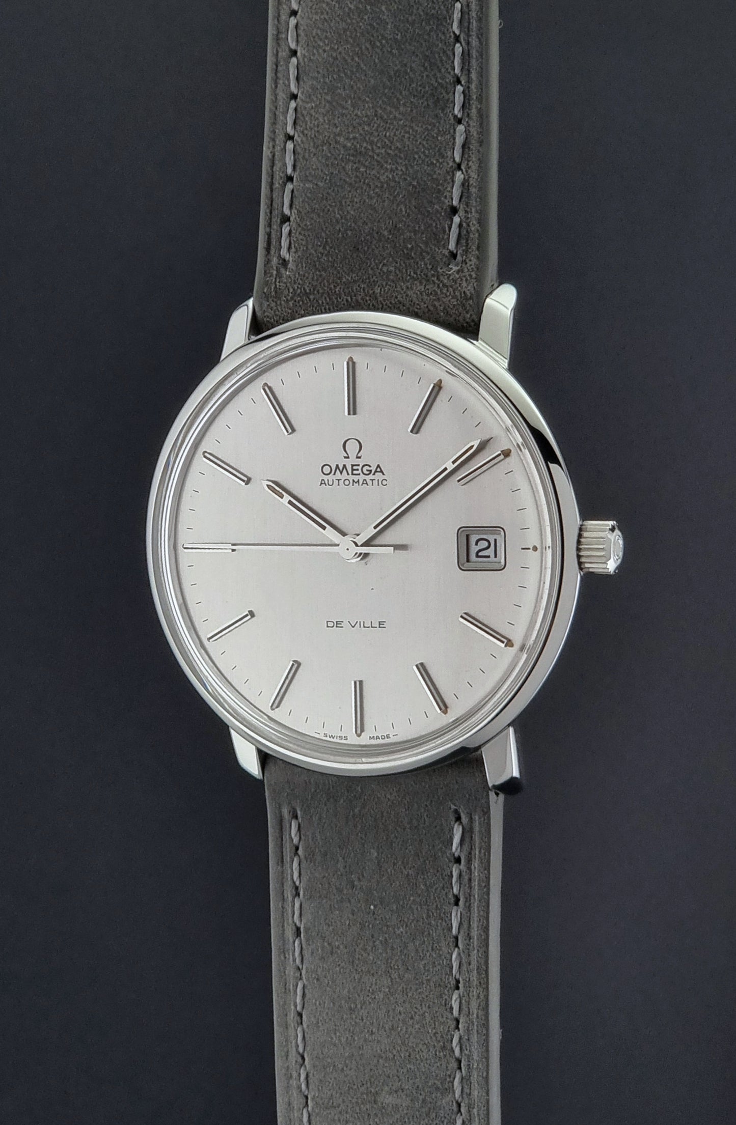 Vintage Omega De-ville 166.0134 wristwatch with a silver dial and dark leather strap on a gray background crown profile