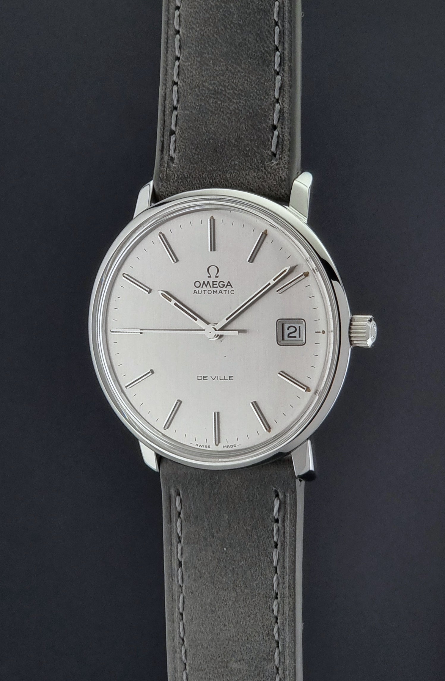 Vintage Omega De-ville 166.0134 wristwatch with a silver dial and dark leather strap on a gray background crown profile