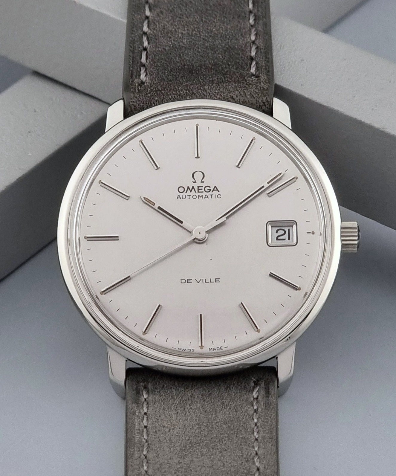 Vintage Omega De-ville 166.0134 wristwatch with a silver dial and dark leather strap on a gray background close up dial view