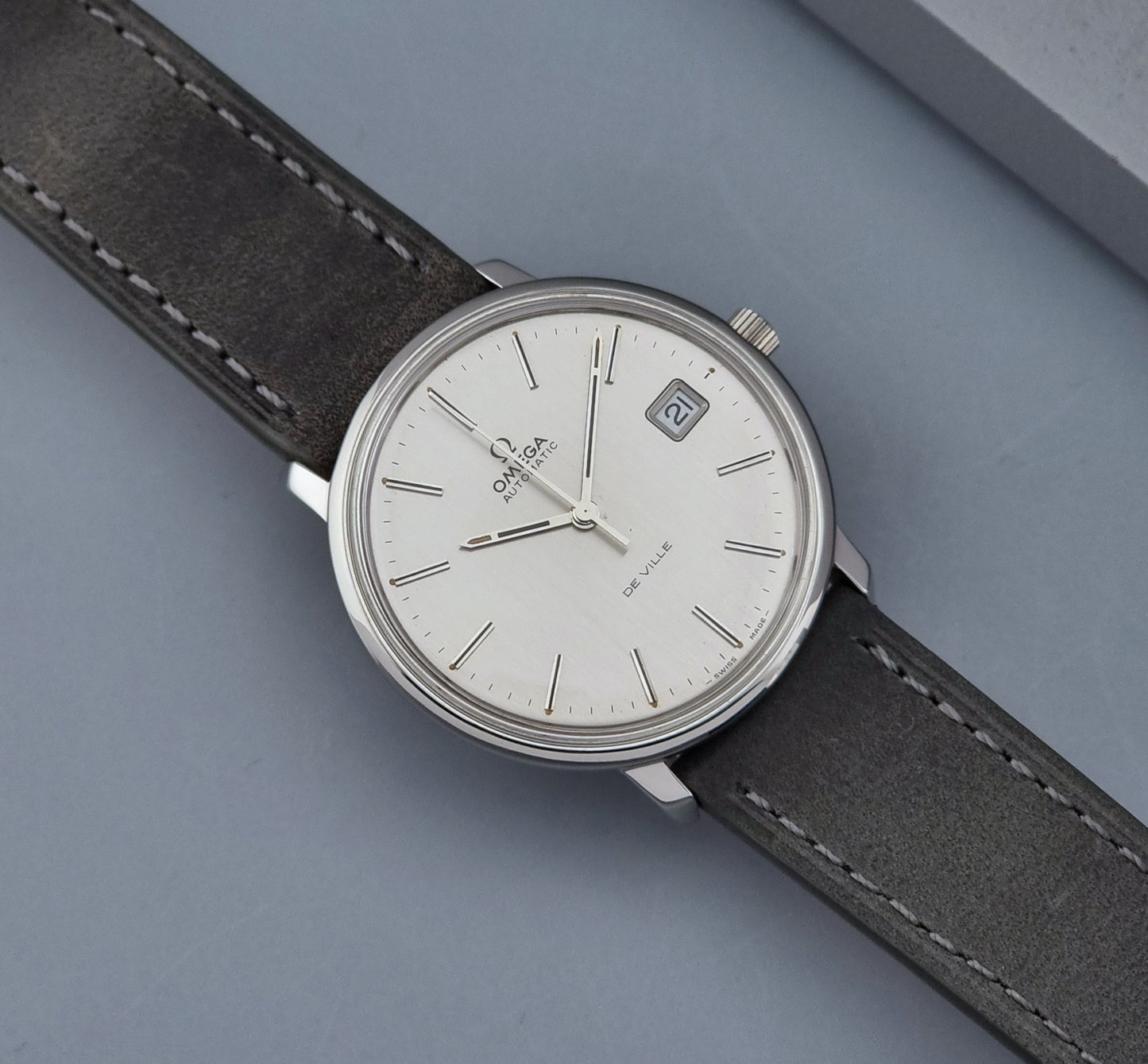 Vintage Omega De-ville 166.0134 wristwatch with a silver dial and dark leather strap on a gray background