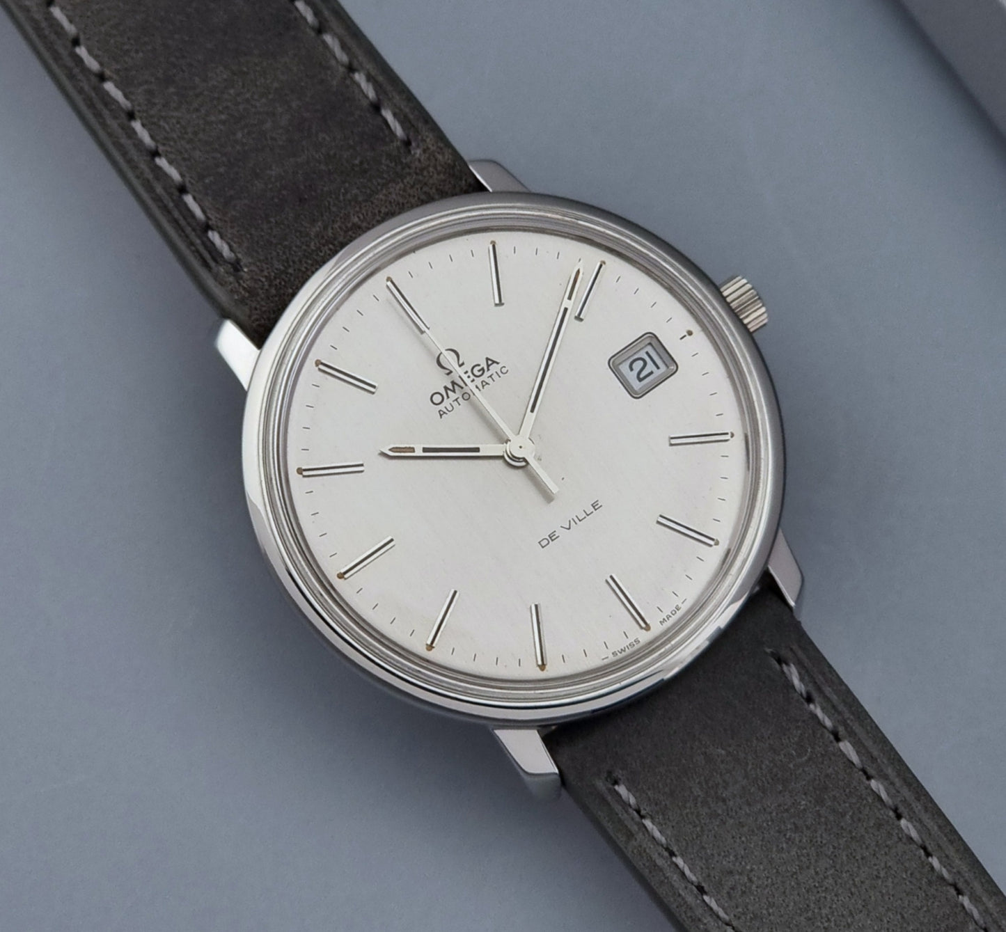 Vintage Omega De-ville 166.0134 wristwatch with a silver dial and dark leather strap on a gray background close up