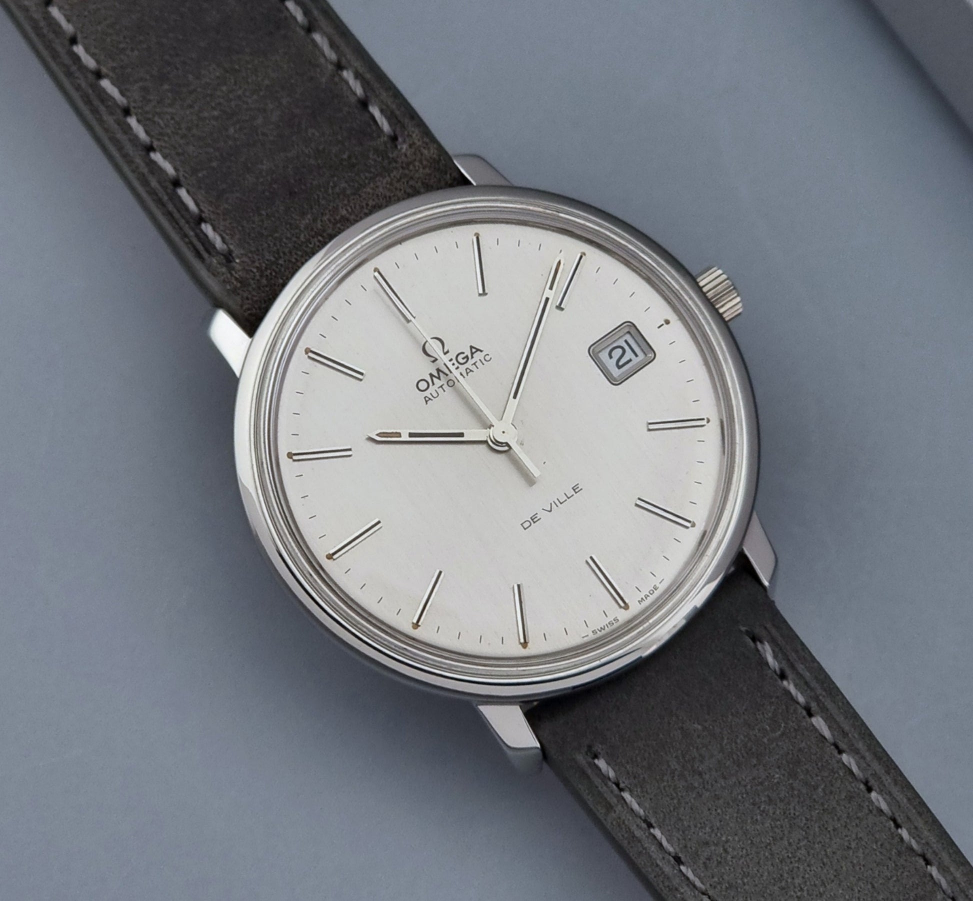 Vintage Omega De-ville 166.0134 wristwatch with a silver dial and dark leather strap on a gray background close up