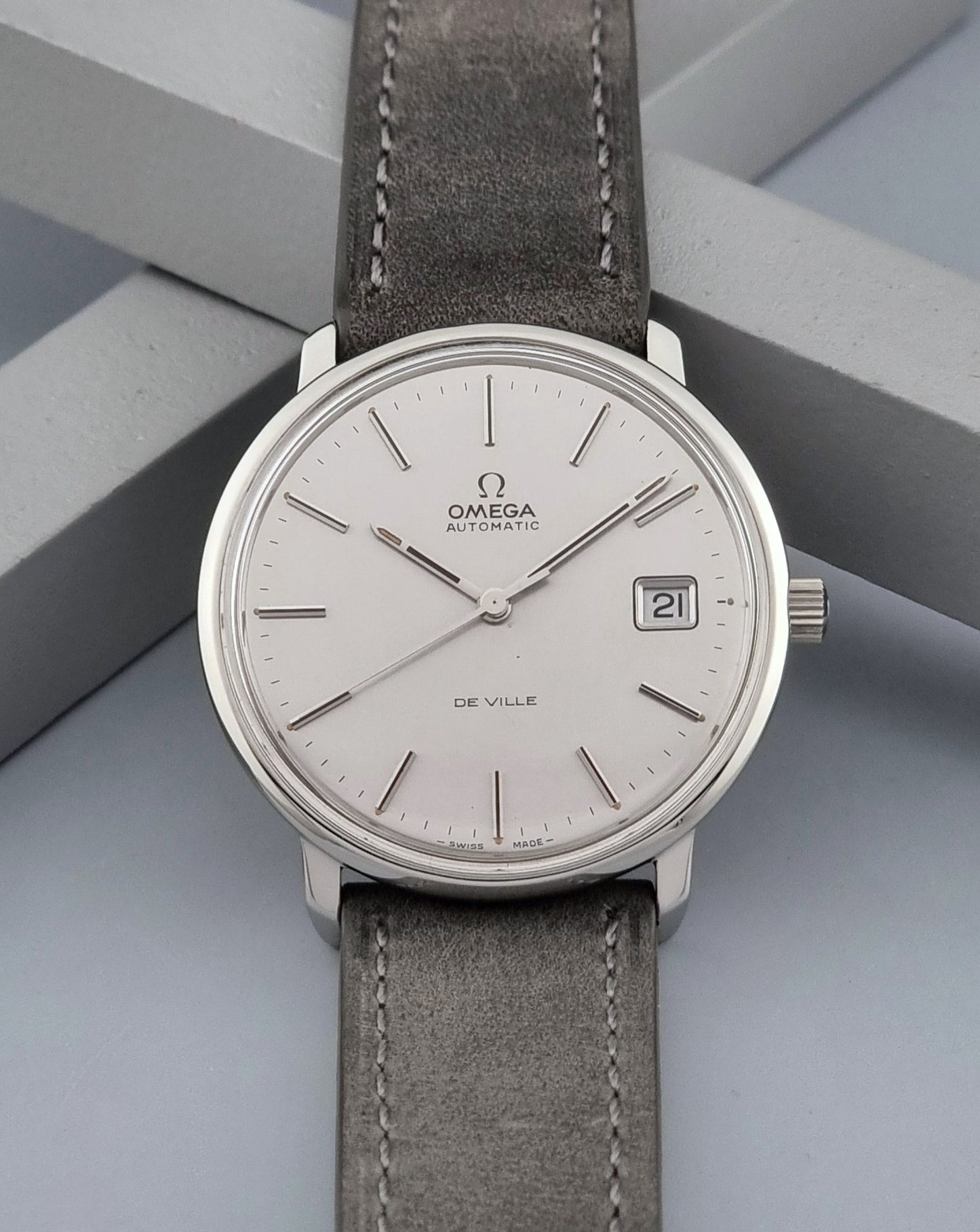 Vintage Omega De-ville 166.0134 wristwatch with a silver dial and dark leather strap on a gray background front view
