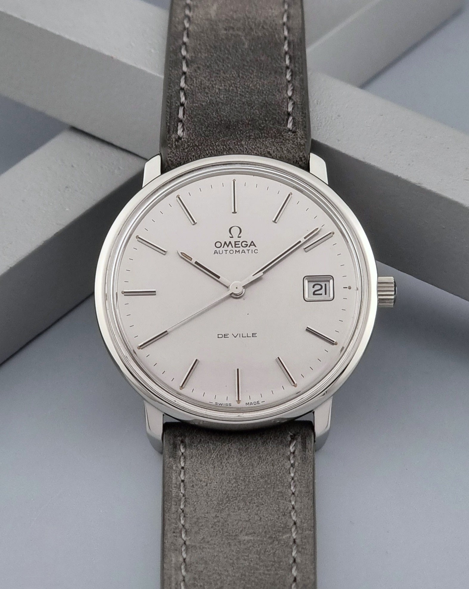 Vintage Omega De-ville 166.0134 wristwatch with a silver dial and dark leather strap on a gray background front view