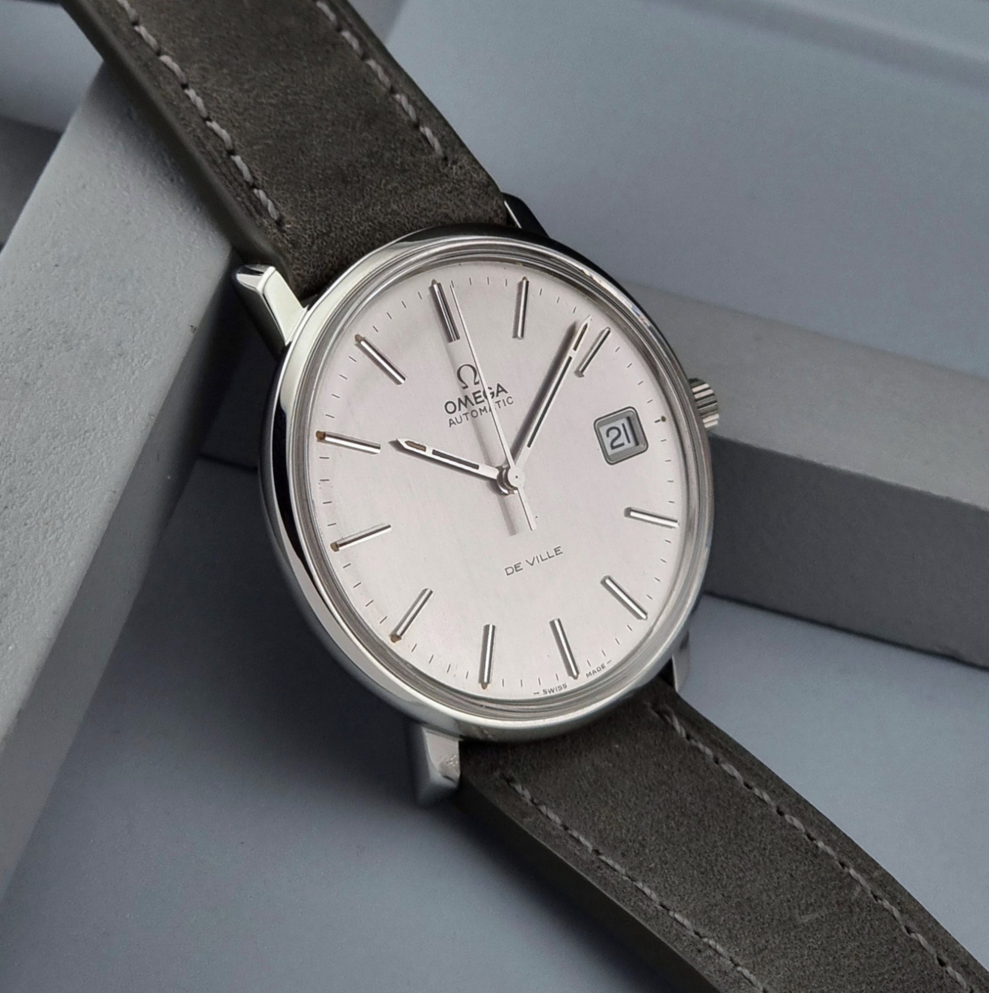 Vintage Omega De-ville 166.0134 wristwatch with a silver dial and dark leather strap on a gray background side view