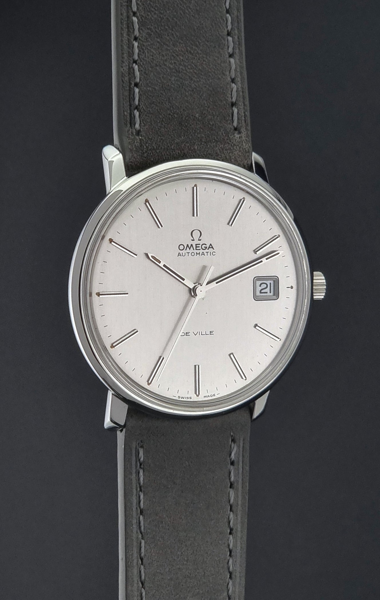 Vintage Omega De-ville 166.0134 wristwatch with a silver dial and dark leather strap on a gray background side profile