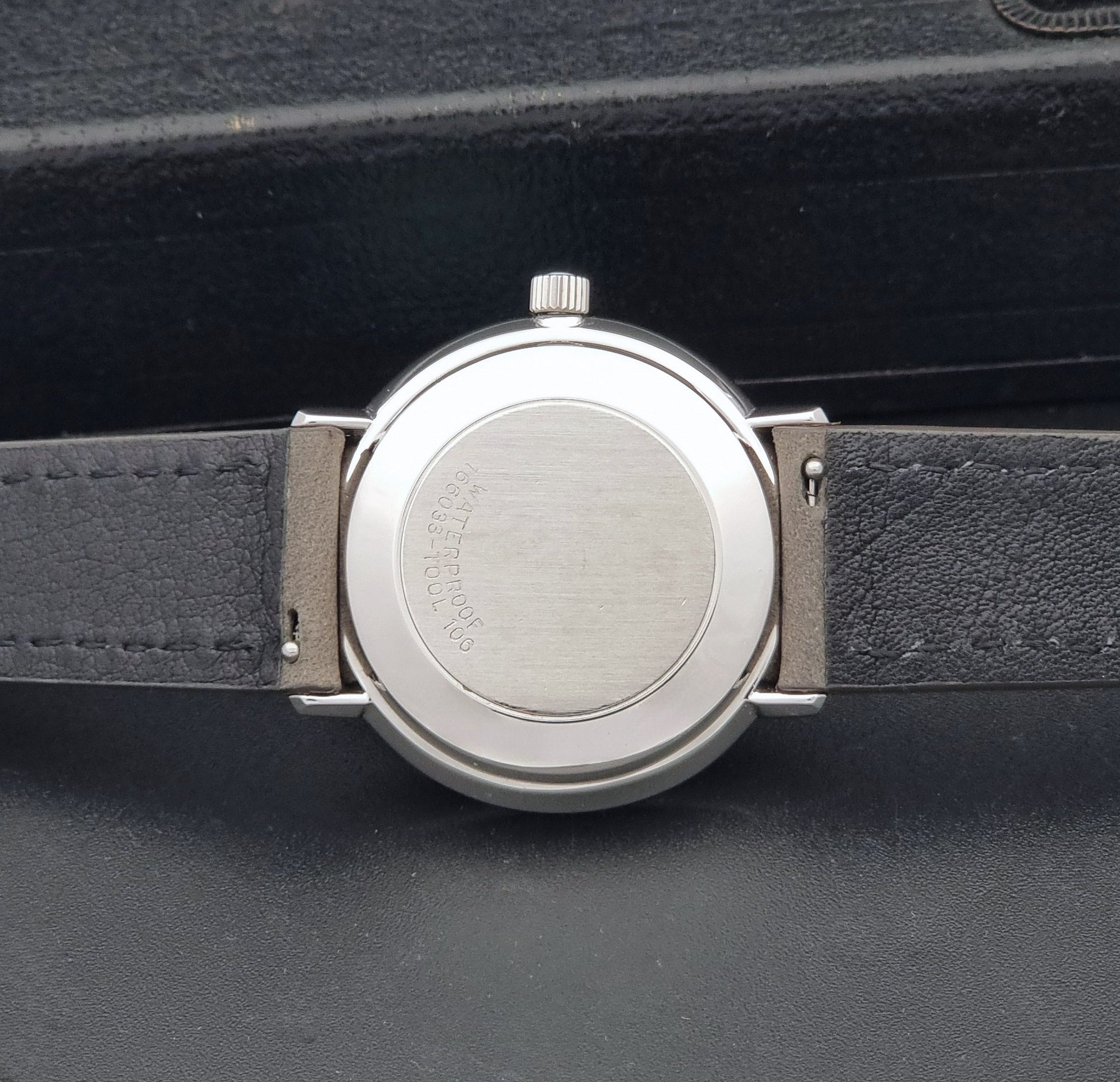 Vintage Omega De-Ville 166.033 Wristwatch with gray strap and white dial on a dark background case back view