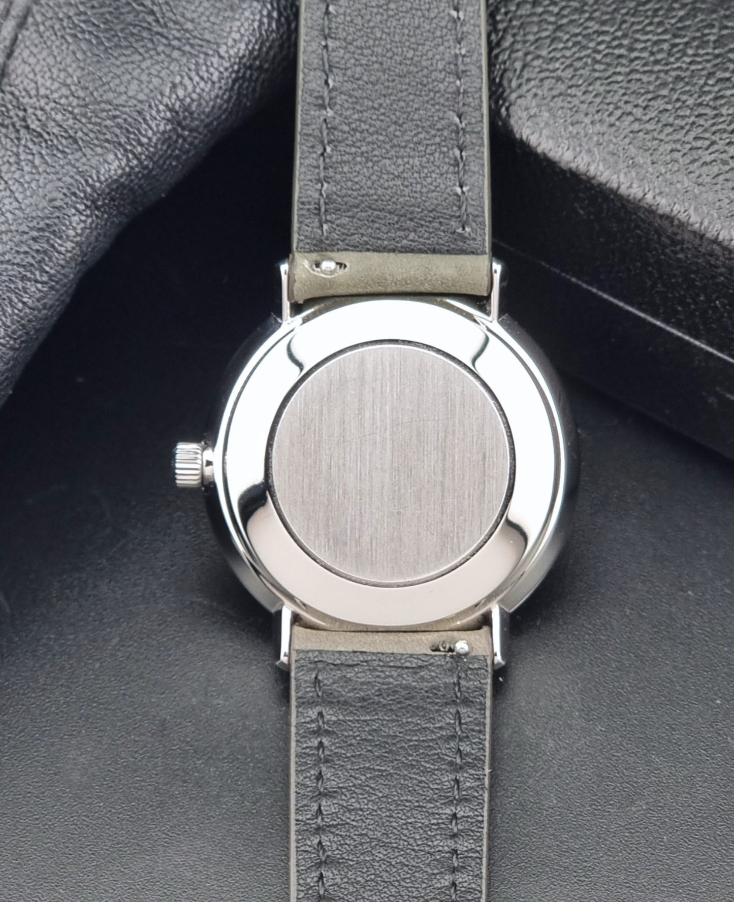 Vintage Omega De-Ville 166.033 Wristwatch with a date window, attached to a gray leather strap, photographed on a dark gray surface case back view