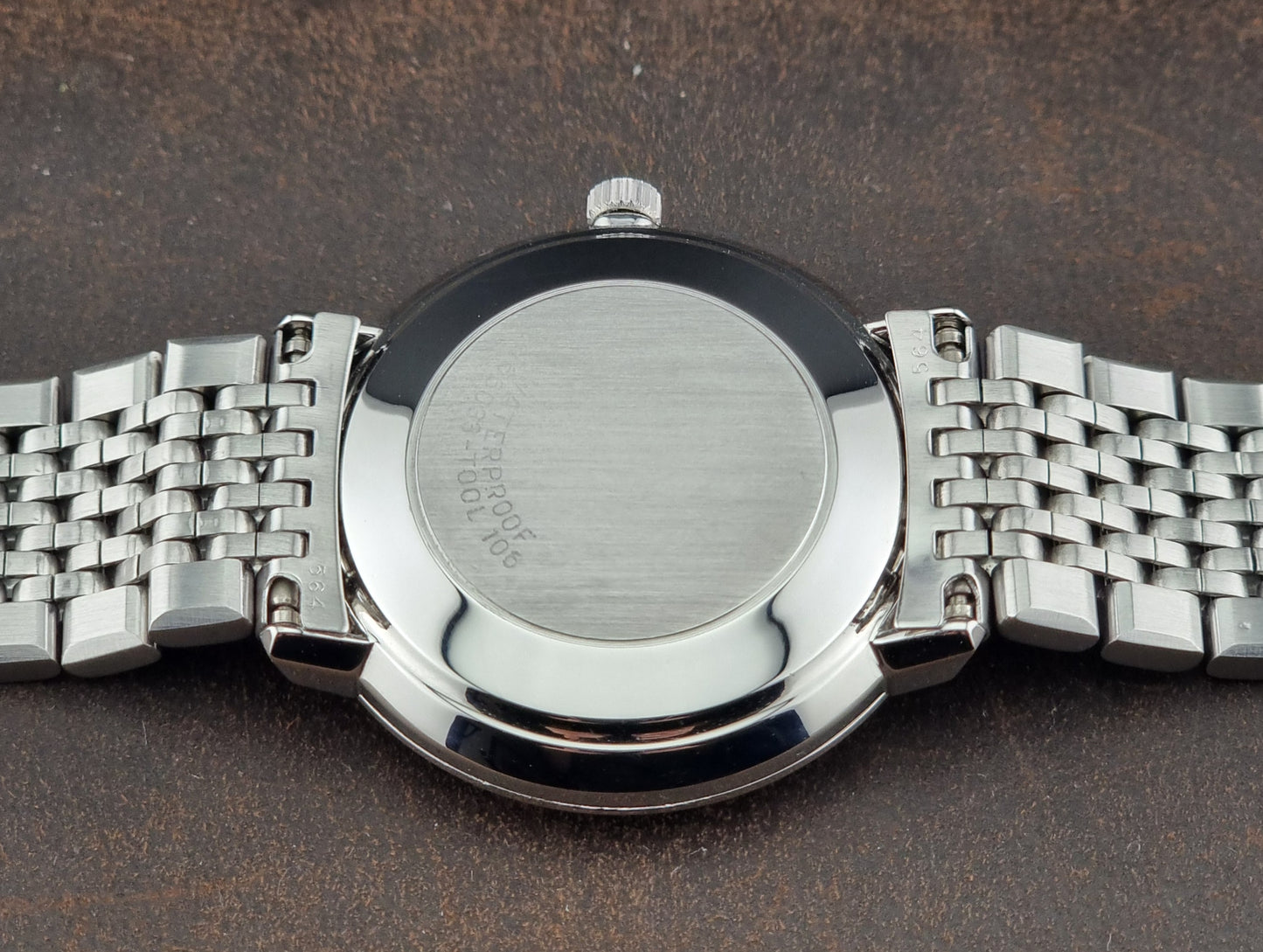Close-up of a Vintage Omega De Ville case back with a metallic band on a dark background