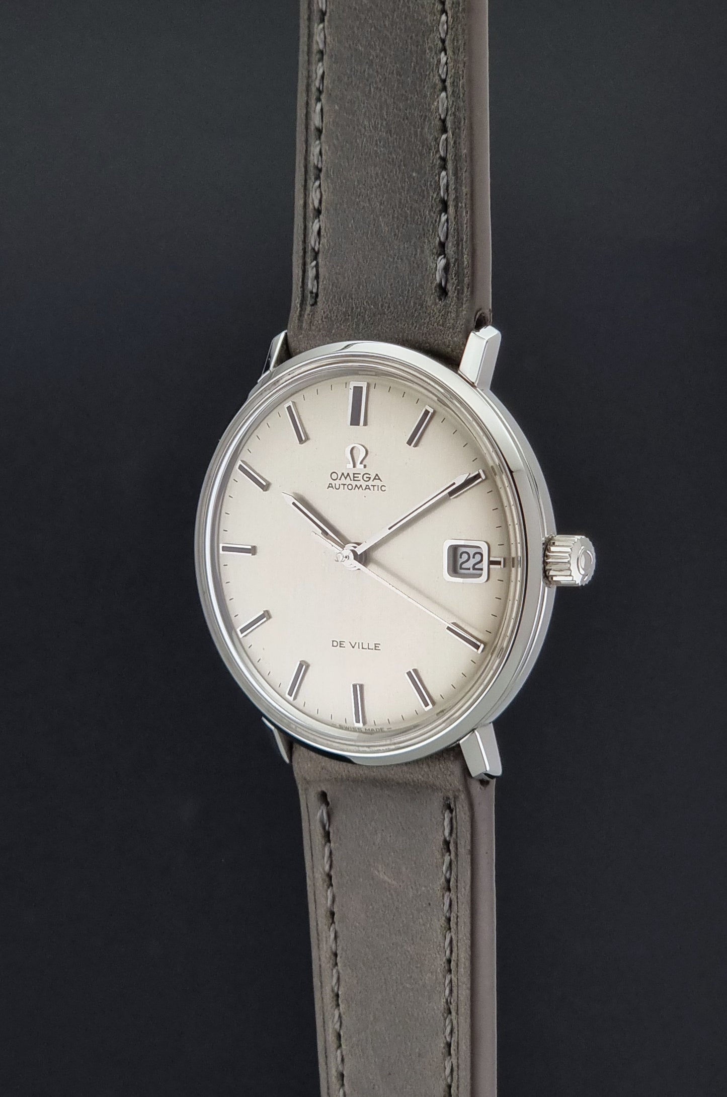 Vintage Omega De-Ville 166.033 Wristwatch with gray strap and white dial on a dark background crown profile view