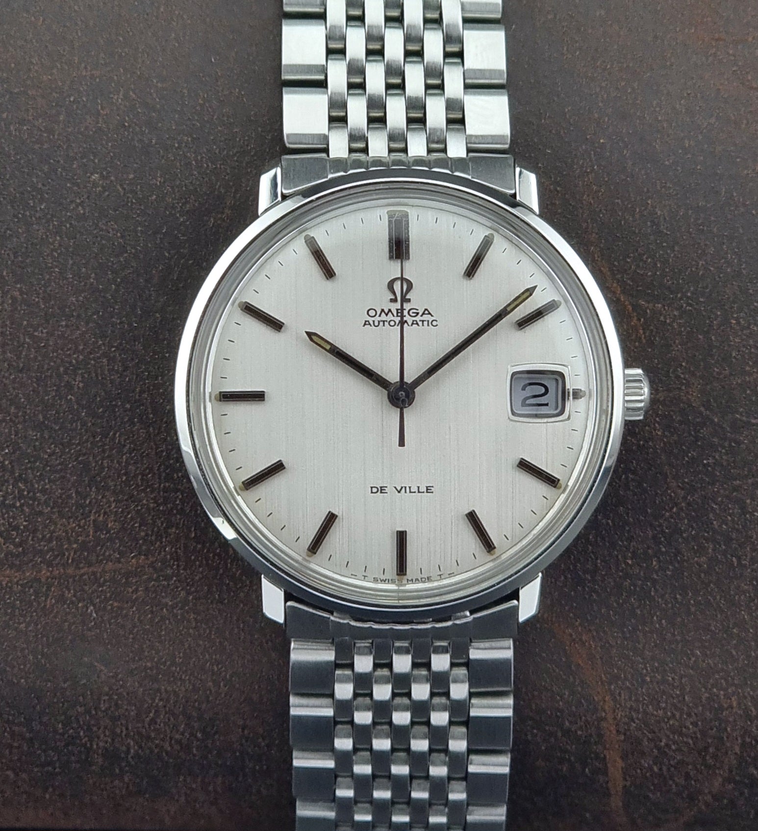 Vintage Omega De Ville watch with a white face on a dark brown background