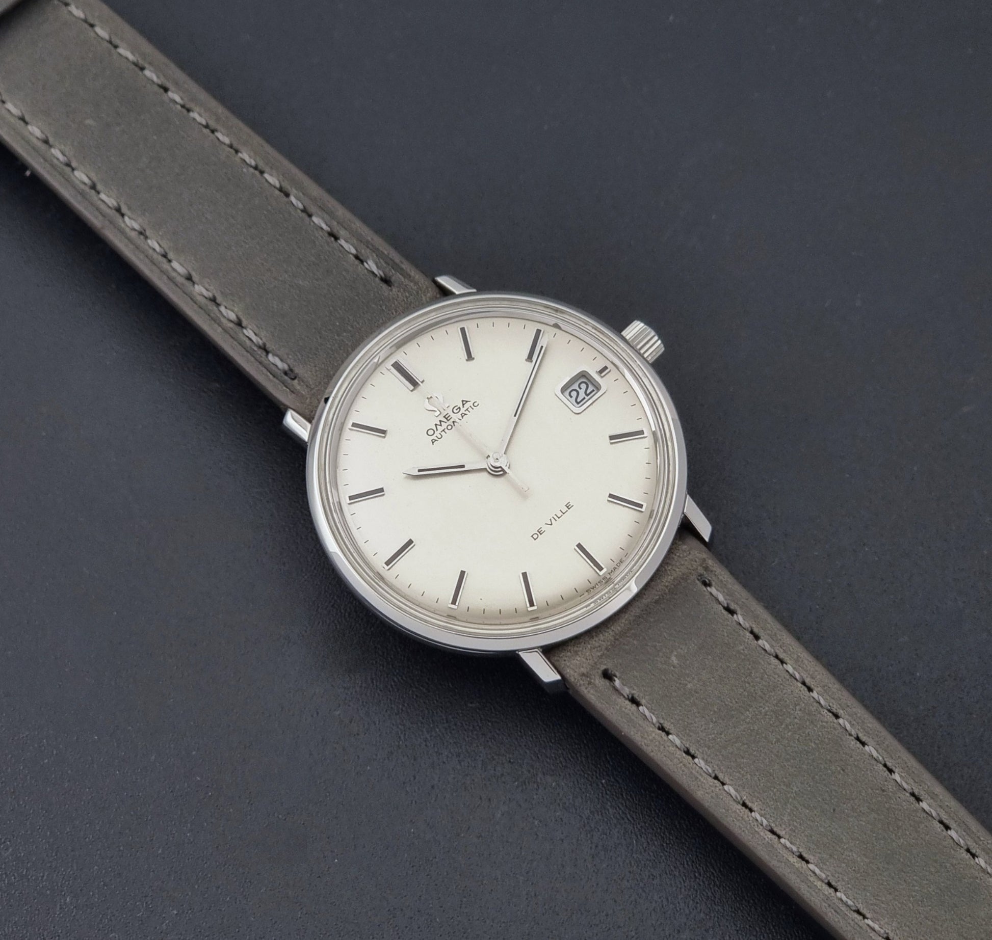 Vintage Omega De-Ville 166.033 Wristwatch with gray strap and white dial on a dark background dial