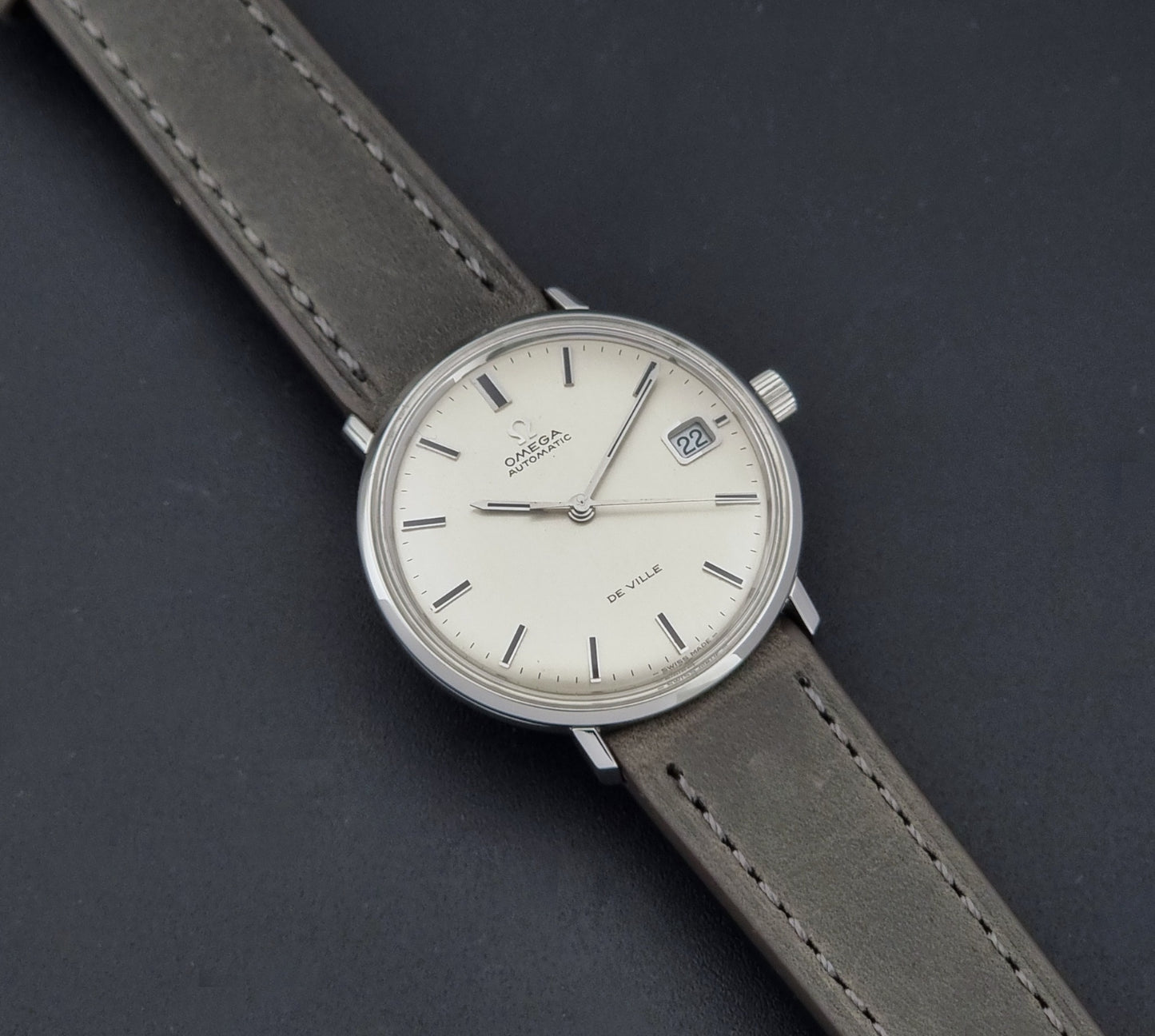 Vintage Omega De-Ville 166.033 Wristwatch with gray strap and white dial on a dark background close up dial view