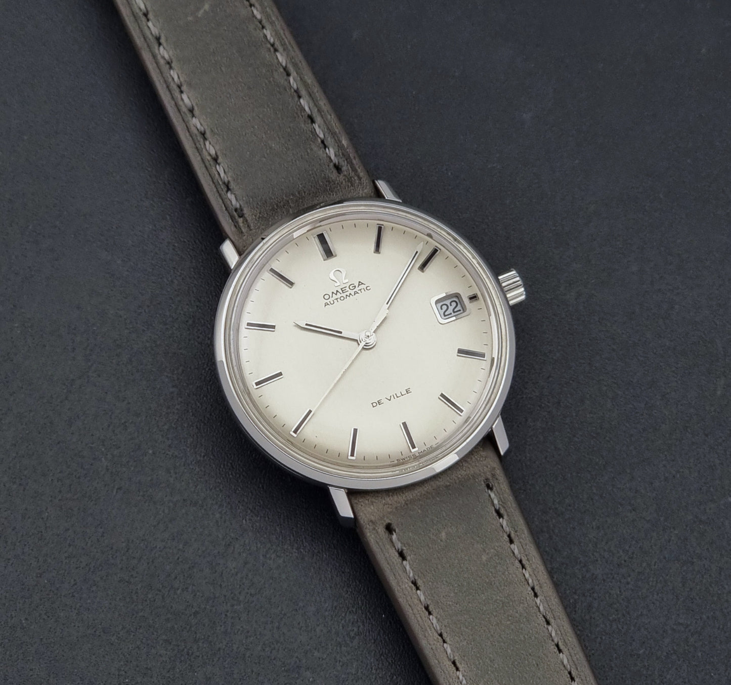Vintage Omega De-Ville 166.033 Wristwatch with gray strap and white dial on a dark background front view