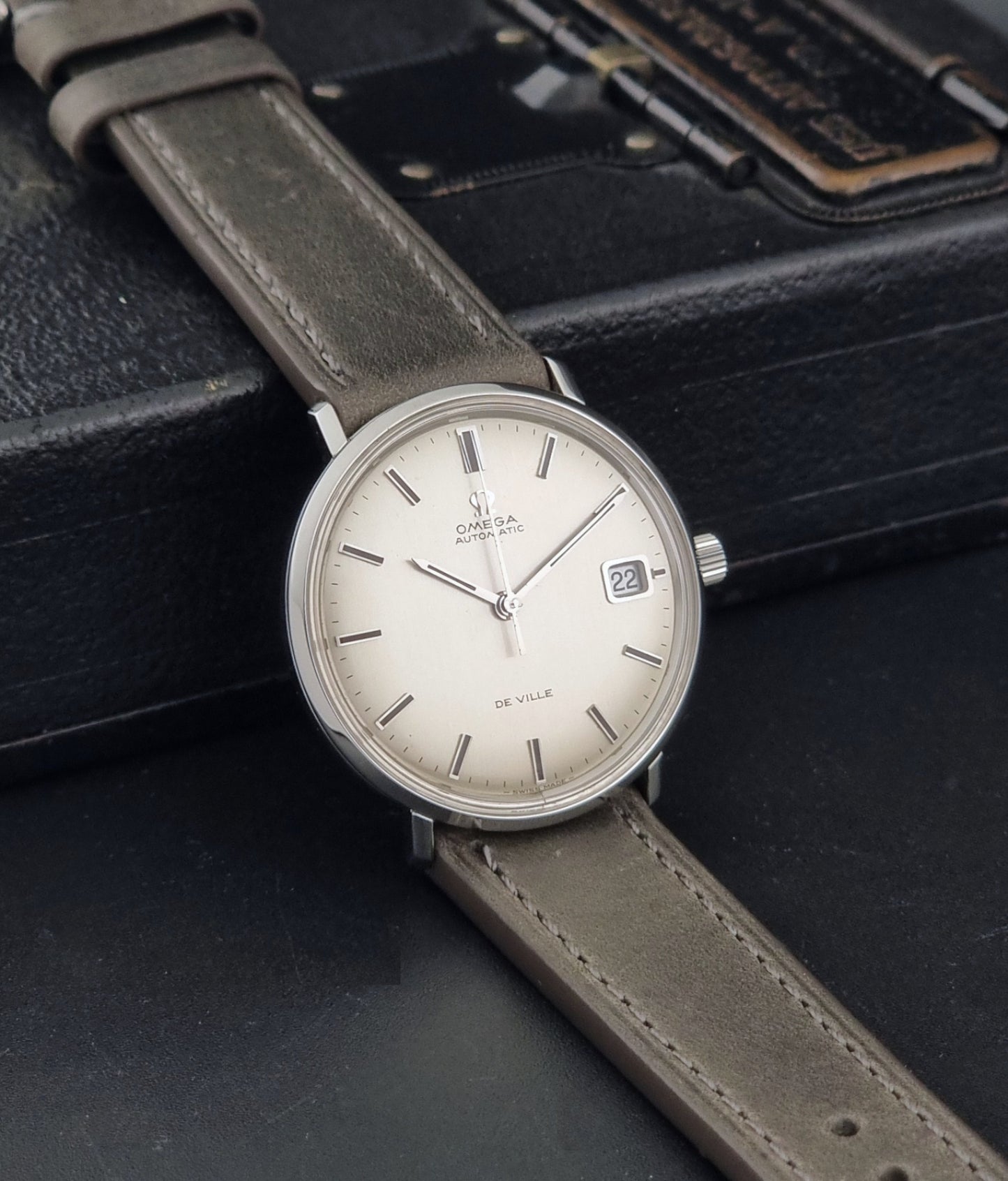 Vintage Omega De-Ville 166.033 Wristwatch with gray strap and white dial on a dark background side view