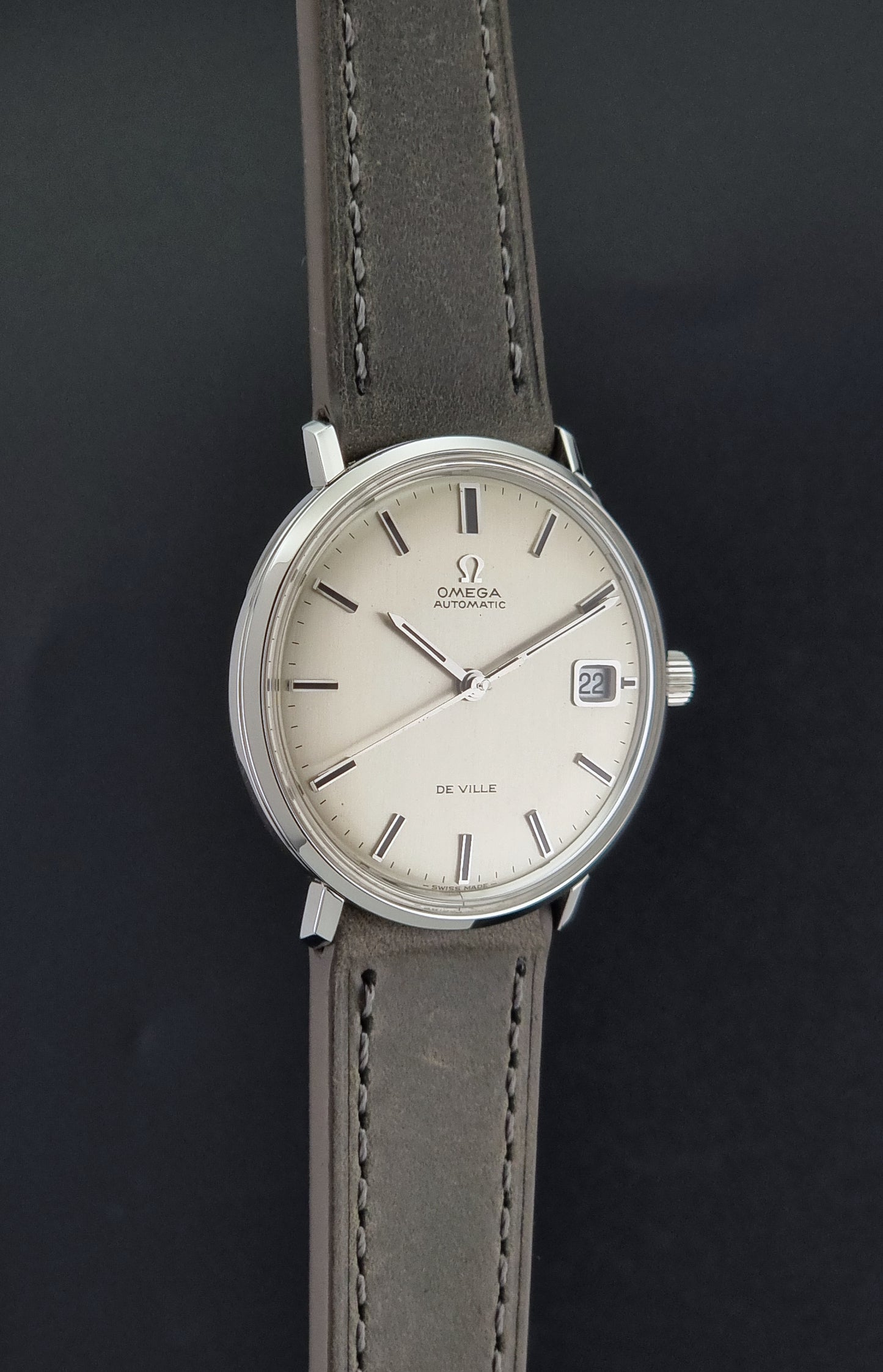 Vintage Omega De-Ville 166.033 Wristwatch with gray strap and white dial on a dark background side profile view