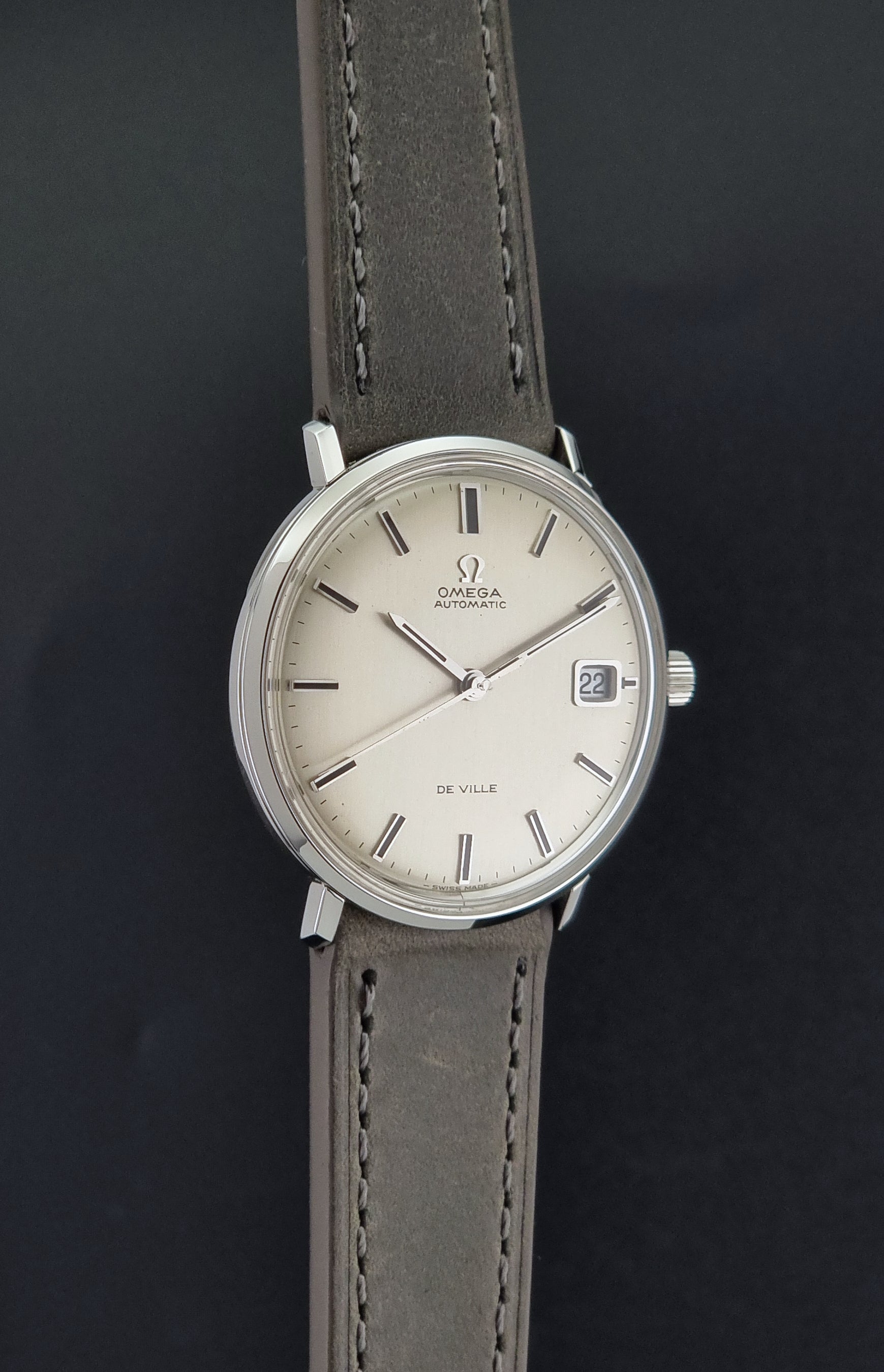 Vintage Omega De-Ville 166.033 Wristwatch with gray strap and white dial on a dark background side profile view