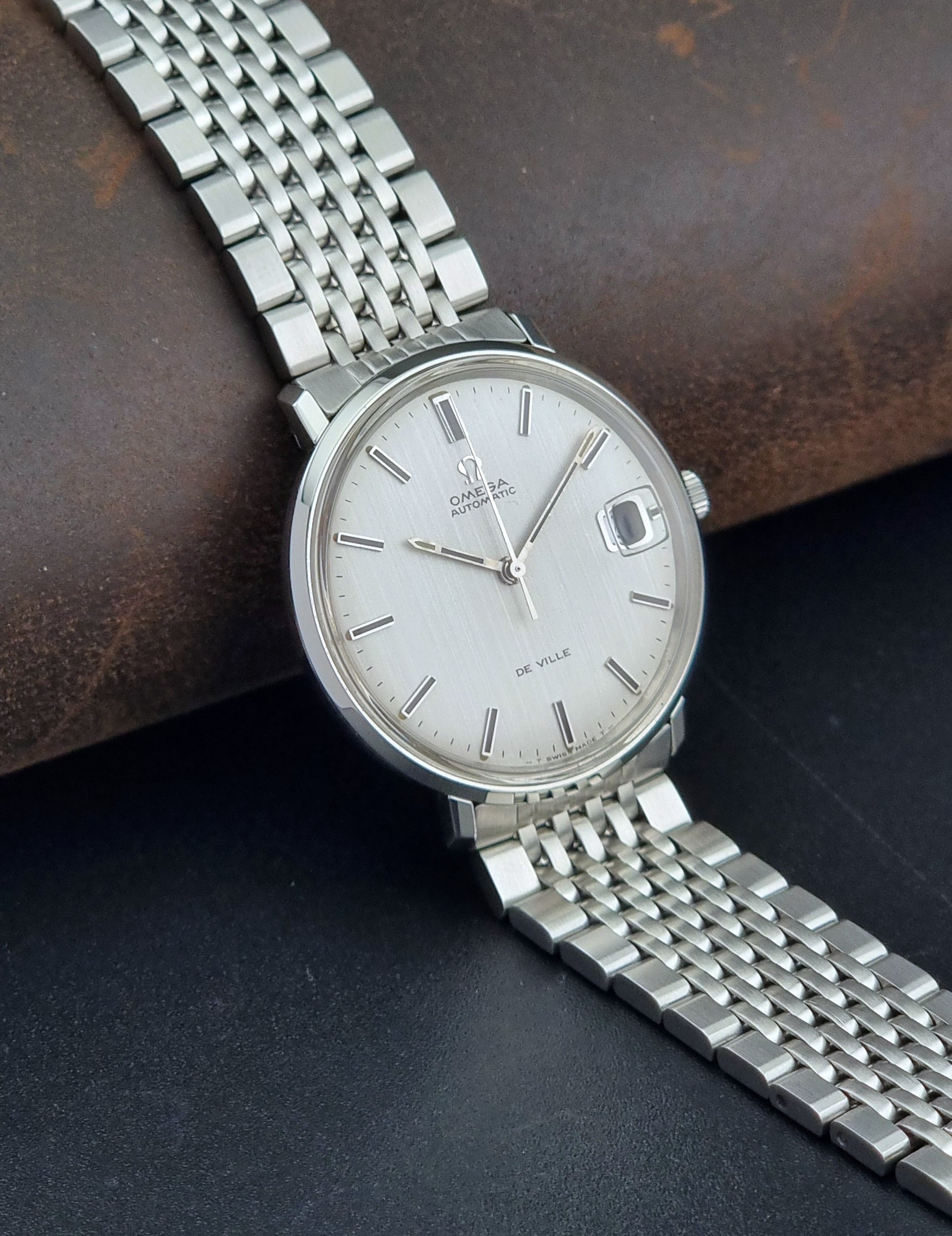 Vintage Omega De Ville watch with a white face on a dark surface