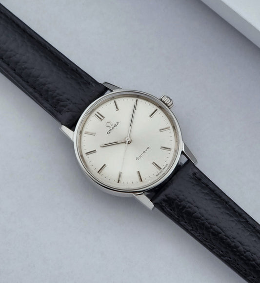 Vintage Omega watch Geneve 135.011 with black strap and silver case on a light gray background dial